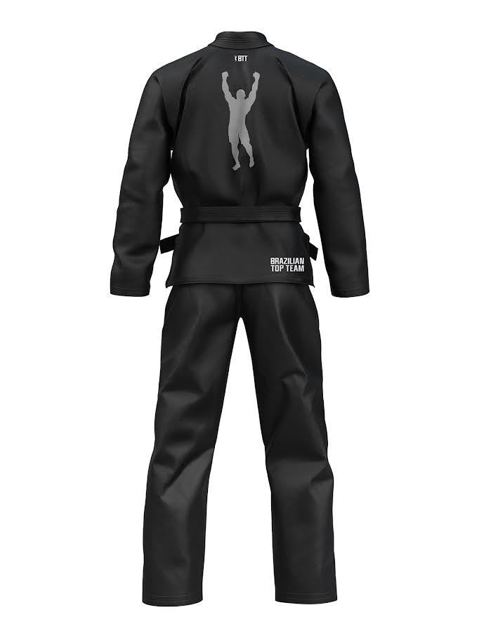 The Kids BTT 25th Anniversary Ultra Lite Black gi is shown from the back, with a silhouette of a person raising their arms on the upper back and “BRAZILIAN TOP TEAM” printed on the lower back.