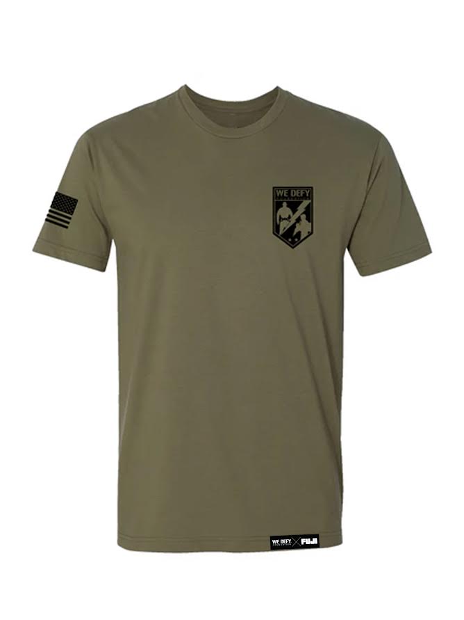 The We Defy Core T-Shirt Military Green features short sleeves, a small flag on the right sleeve, a We Defy shield logo with stars and a grappling image on the left chest, plus small logos at the front bottom hem.