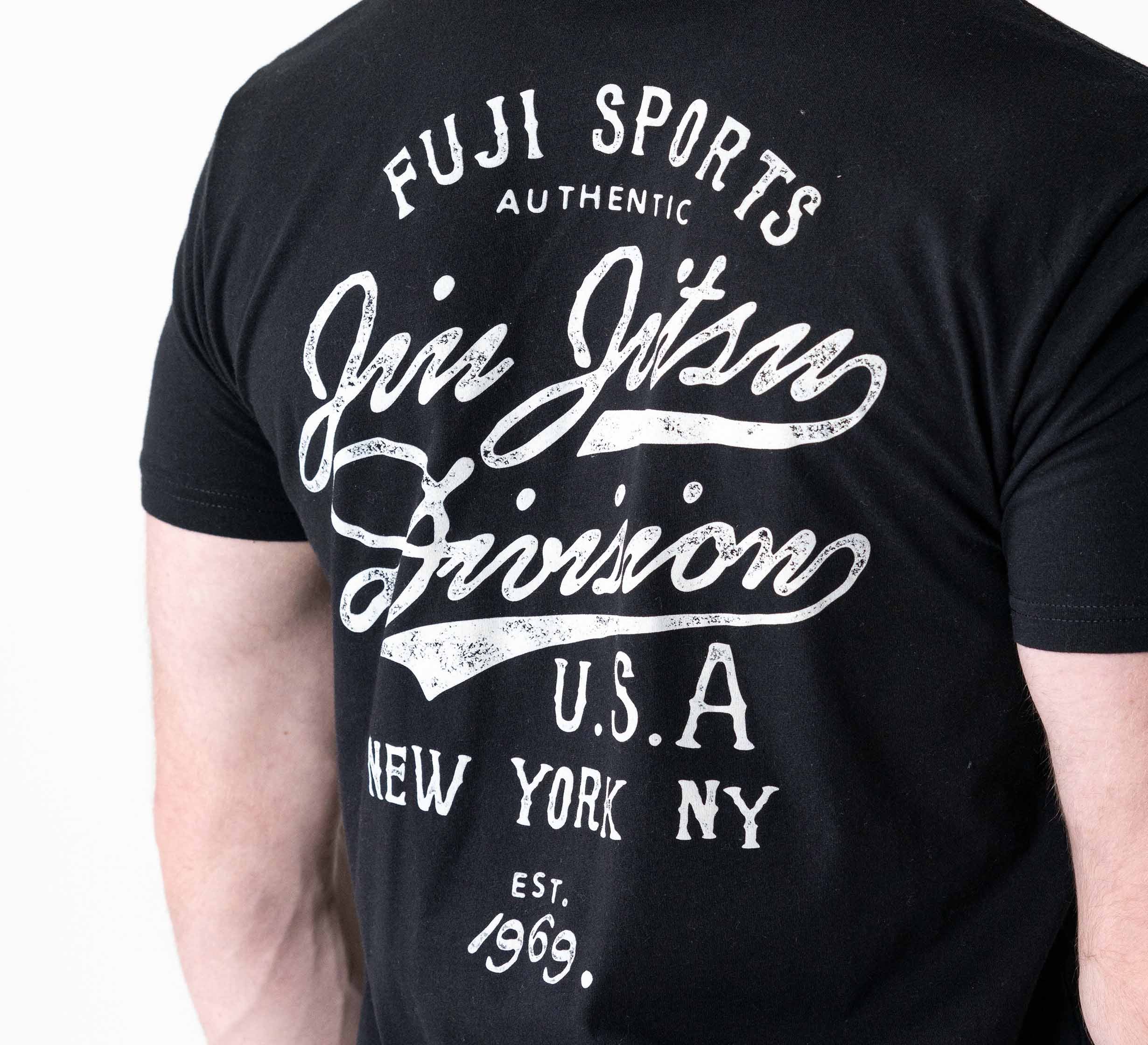 A person is seen from the back wearing the Jiu Jitsu Flow T-Shirt Black, featuring white text: "Fuji Sports Authentic Jiu Jitsu Division U.S.A New York NY Est. 1969," against a plain background.