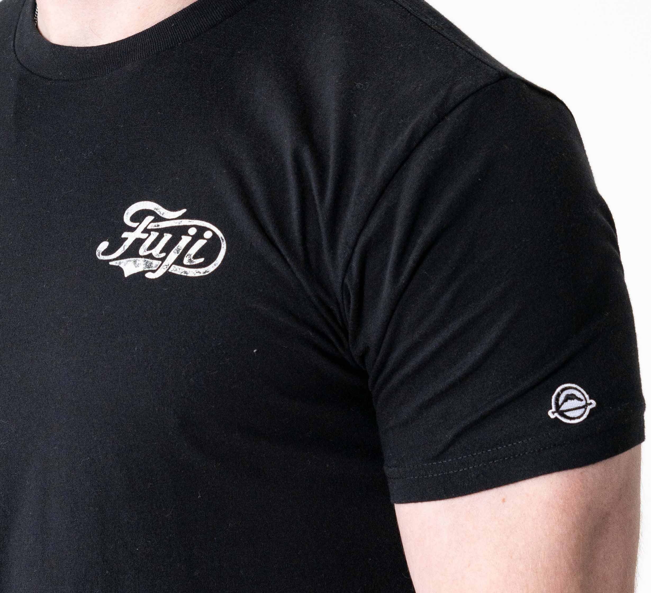 A person wearing the Jiu Jitsu Flow T-Shirt Black featuring "Fuji" in script on the chest and a small circular sleeve logo, shown from shoulders to upper arm.