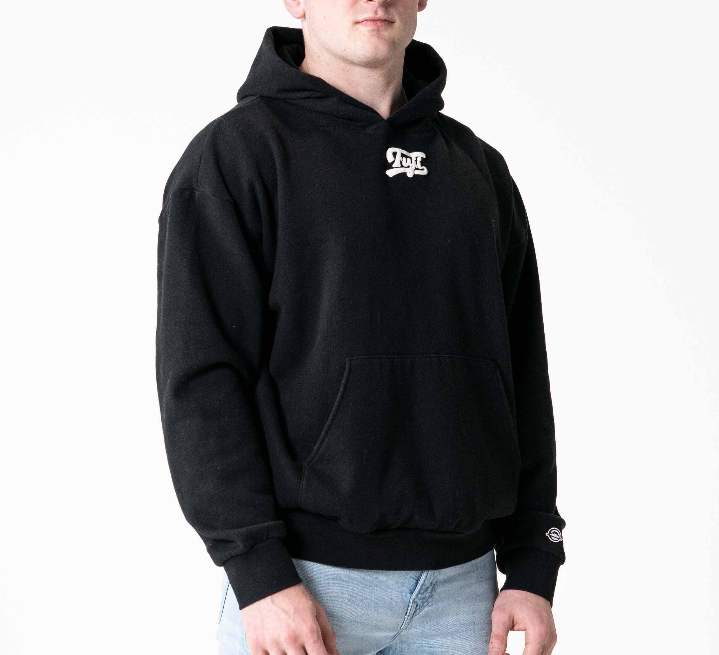 A person wearing the Signature Hoodie Black, featuring a small white chest logo, paired with light blue jeans and standing against a plain white background.