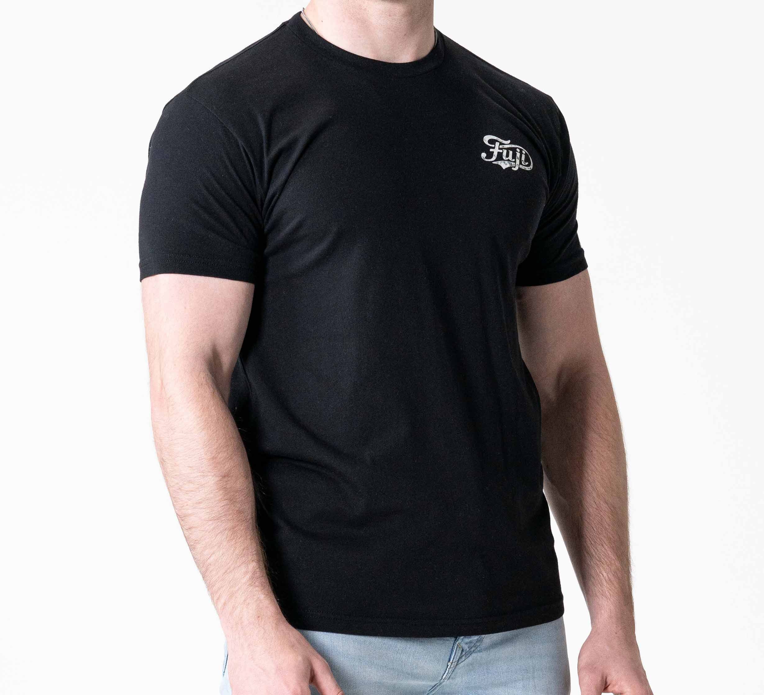 A person wears the Jiu Jitsu Flow T-Shirt Black, featuring a small white Fyll logo on the left chest, paired with light blue jeans and standing against a plain white background.