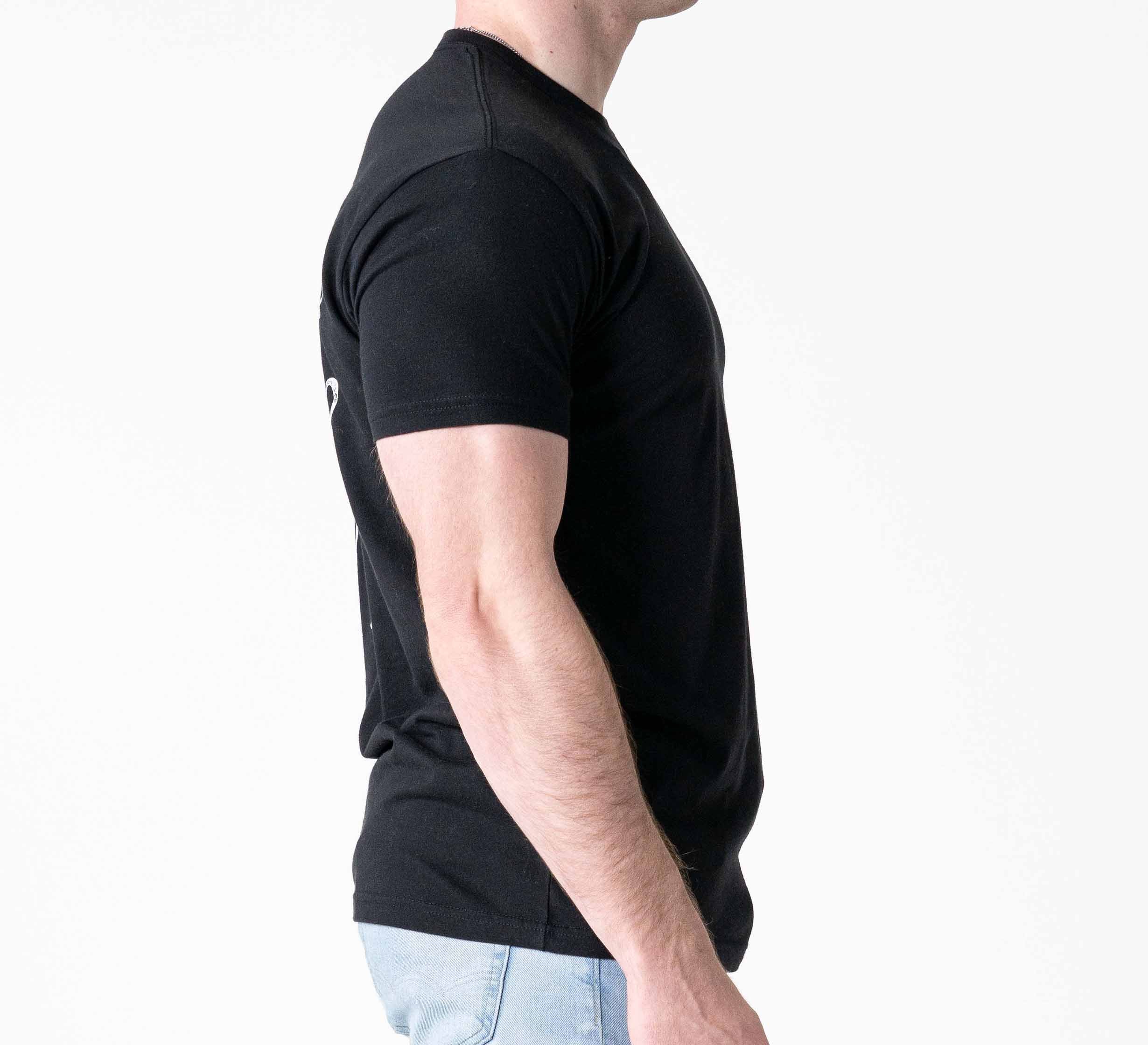 A man wearing a Jiu Jitsu Flow T-Shirt Black and light blue jeans stands in profile against a plain white background.