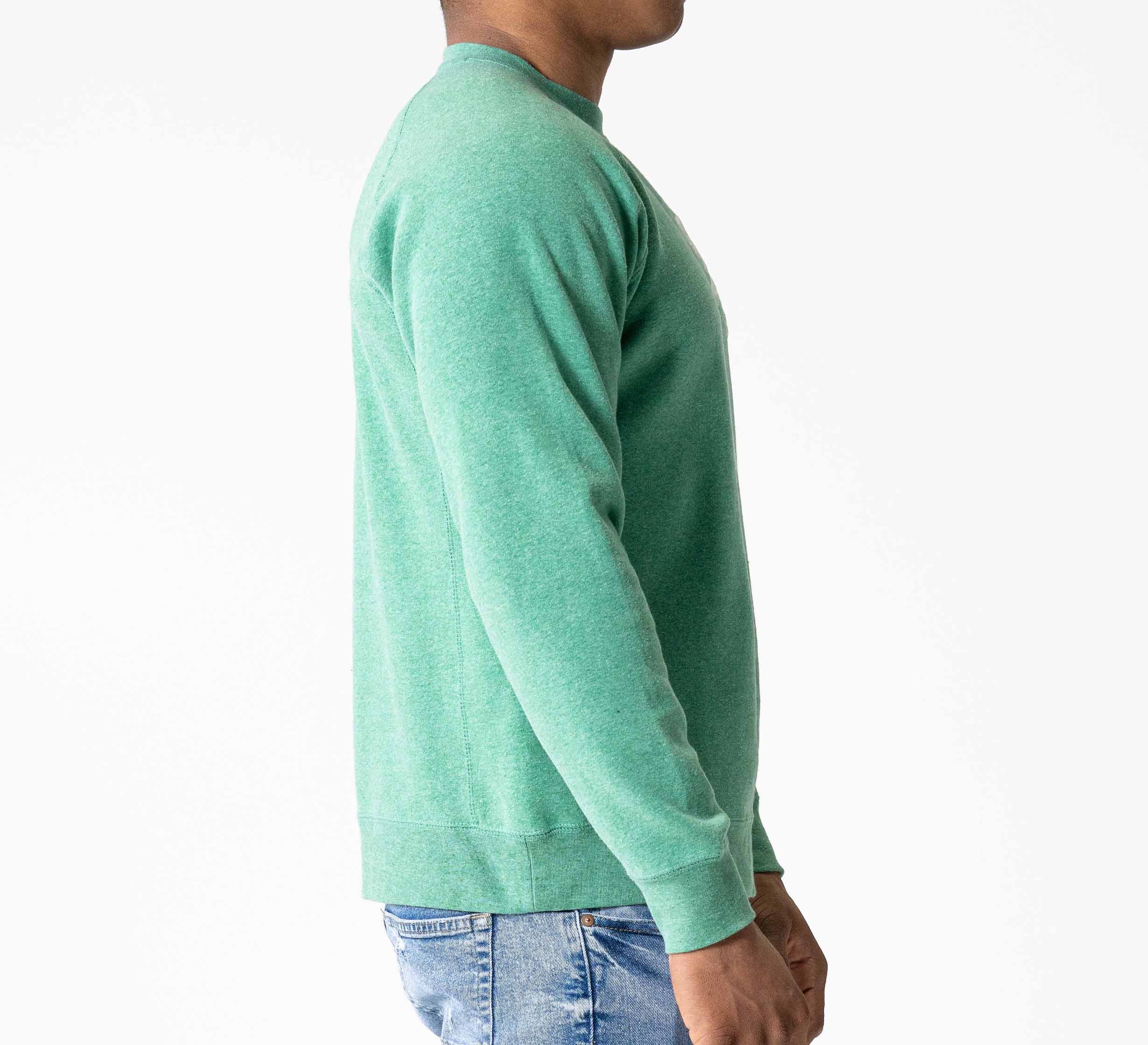 Man standing in profile, wearing the Signature Crewneck Green sweatshirt and blue jeans, against a plain white background.