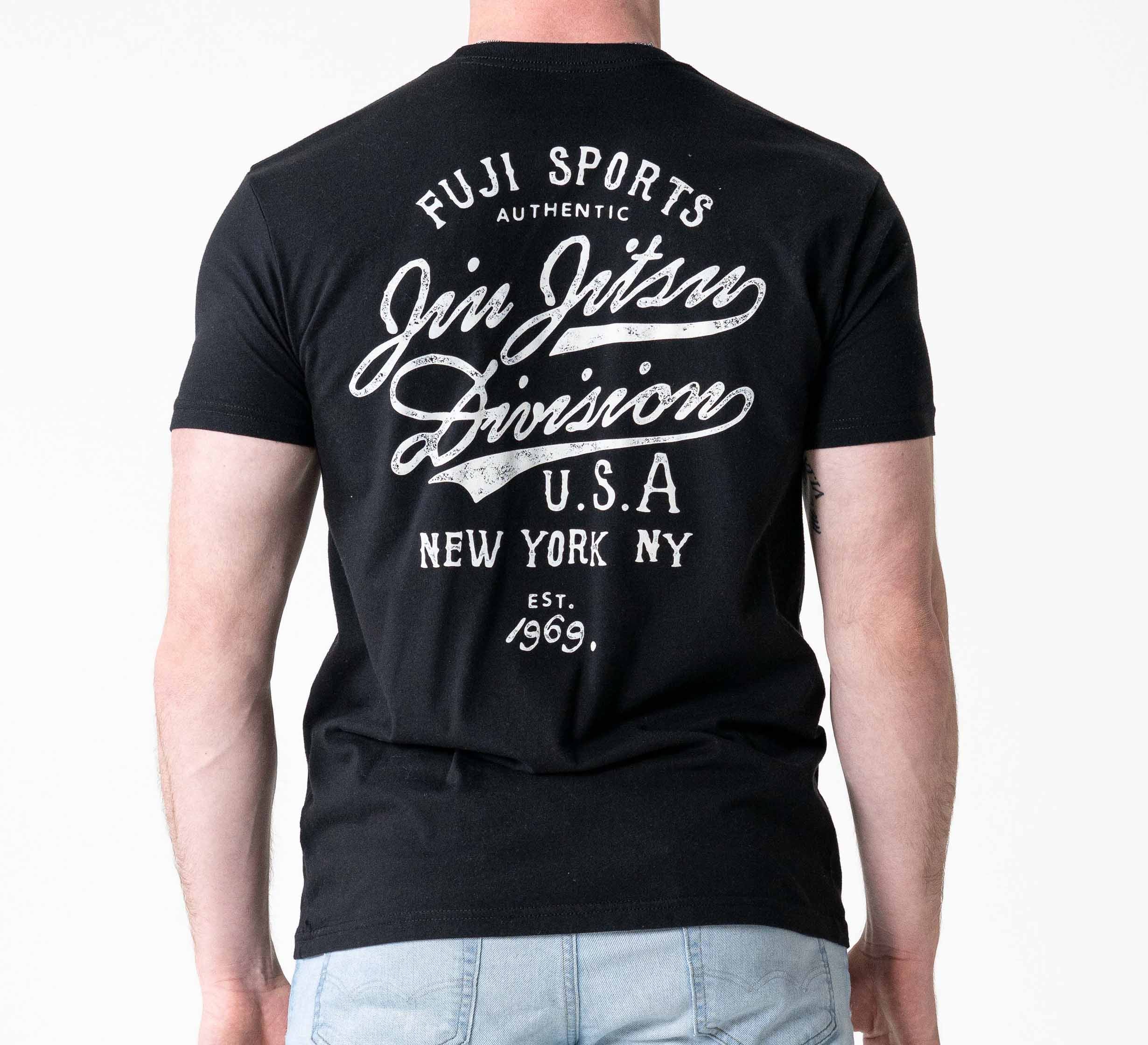 A man is wearing the Jiu Jitsu Flow T-Shirt Black, featuring white text on the back: "Fuji Sports Authentic Jiu Jitsu Division U.S.A New York, NY Est. 1969," while standing against a plain white background.