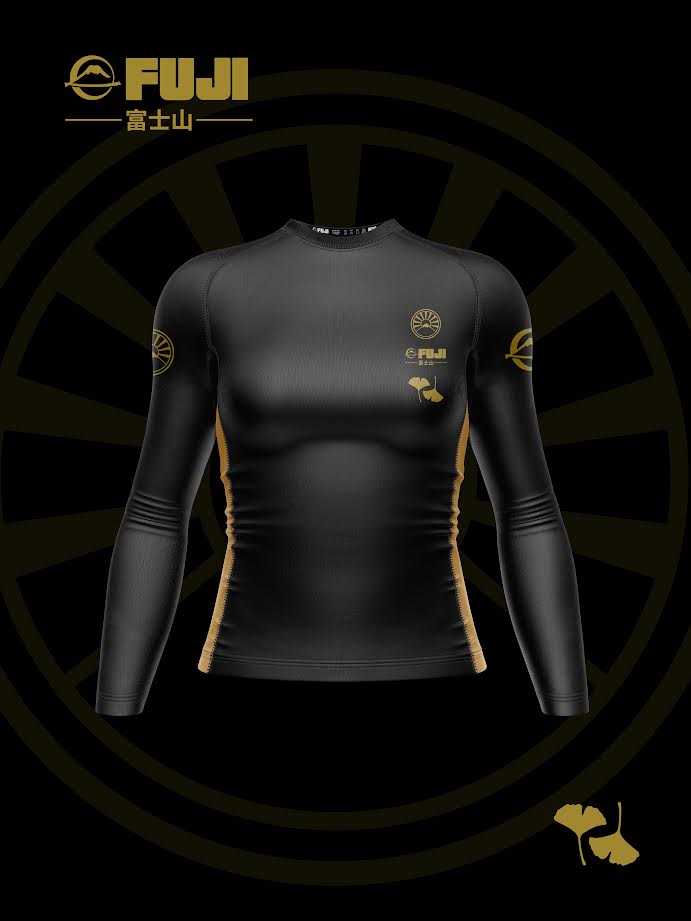 The Womens Heritage Keisho Long Sleeve Rashguard Black is showcased on a black background, featuring gold logos, Japanese text, a stylized ginkgo leaf, and a circular emblem.