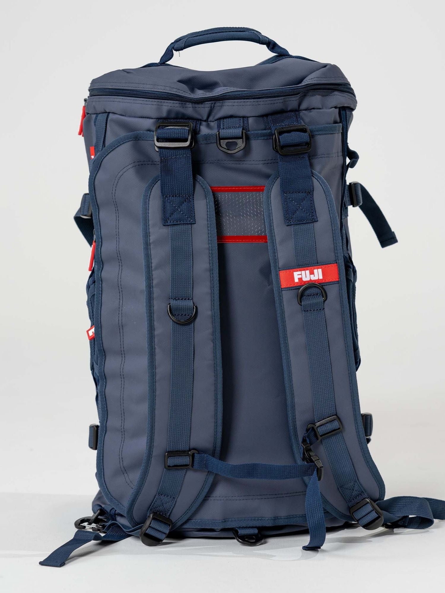 The Comp Convertible Backpack Duffle Navy stands upright on a light background, featuring padded shoulder straps, red accents, multiple adjustment straps, a top handle, and a prominent “FUJI” label.