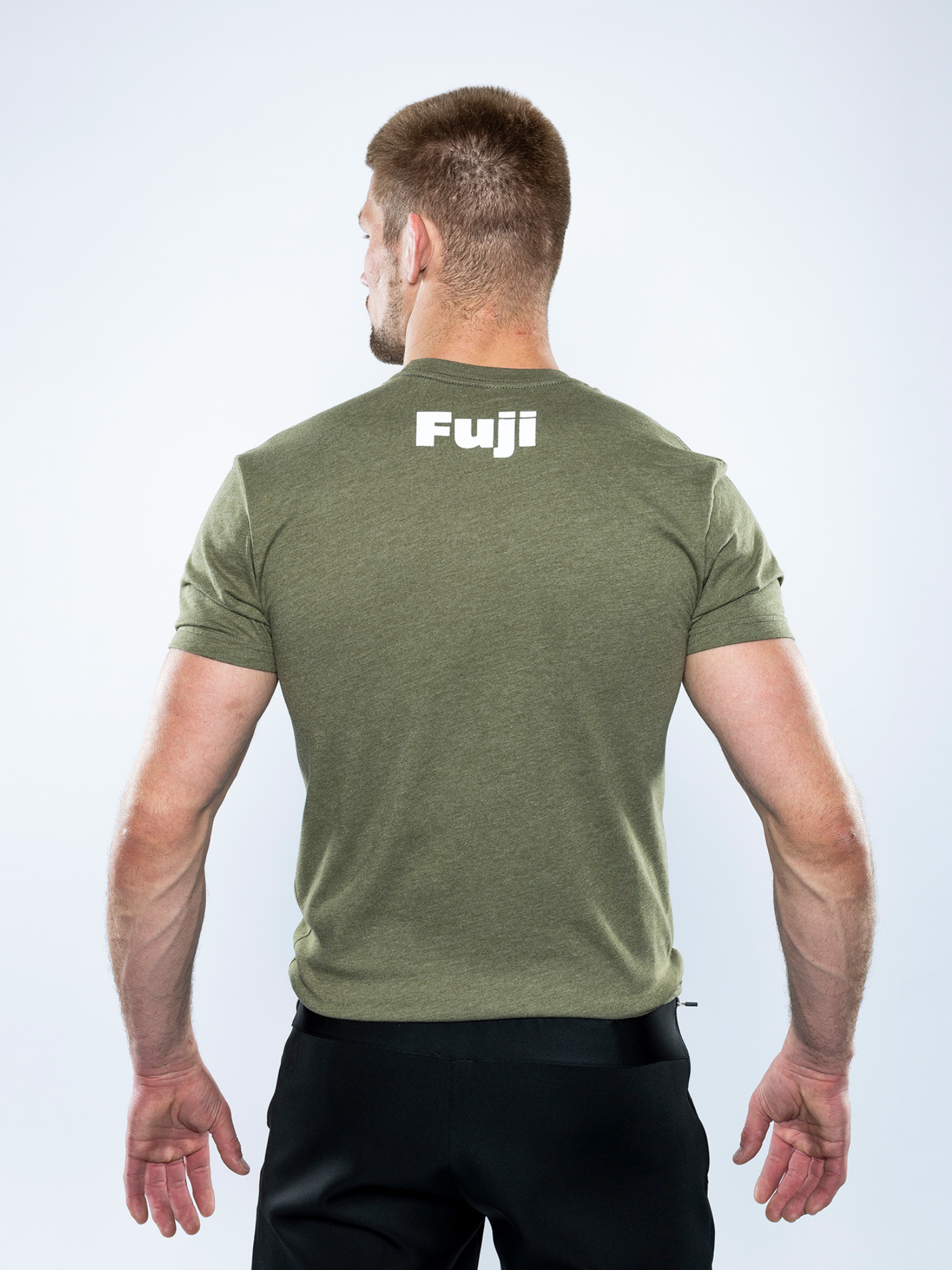 A man with short hair is seen from behind against a white background, wearing the Jiu Jitsu Player T-Shirt in military green with "Fuji" in white on the upper back and black pants.