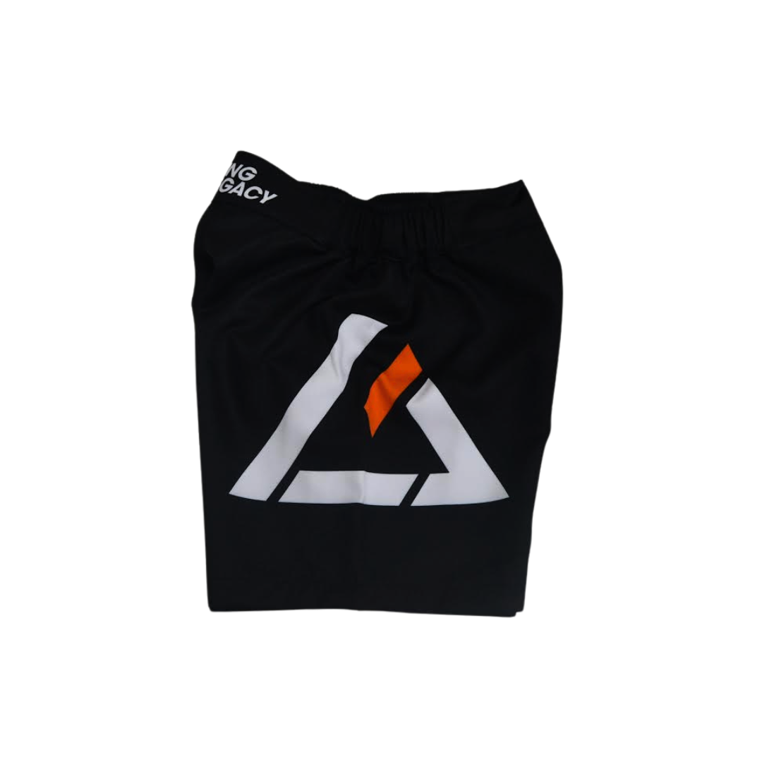 The Rilion Gracie Black Comp Team Shorts are folded, showcasing a bold white and orange geometric logo on the front and partial "NG LEGACY" text on the waistband.