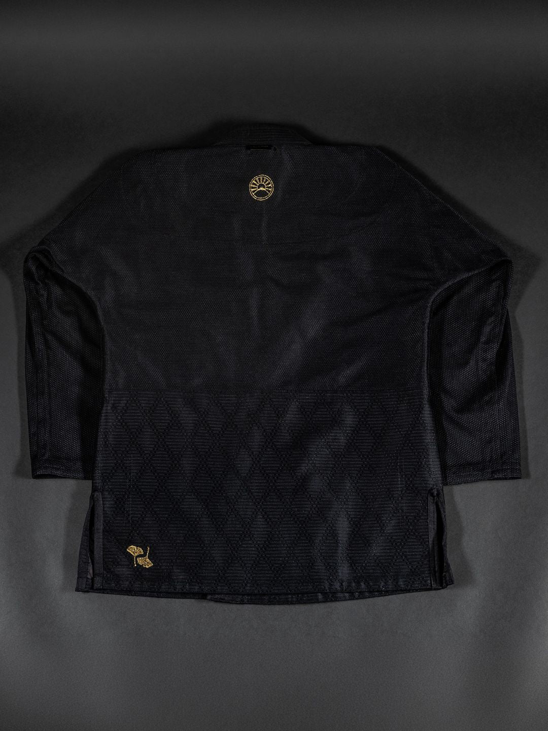 A Womens Heritage Keisho Lightweight BJJ Gi in black, featuring subtle geometric patterns and gold embroidered logos on the upper back and lower side, displayed flat against a dark background.