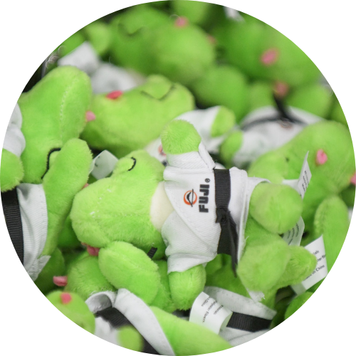 Several small, green plush toys wearing white shirts with the word Fuji printed on them are piled together, filling the frame.
