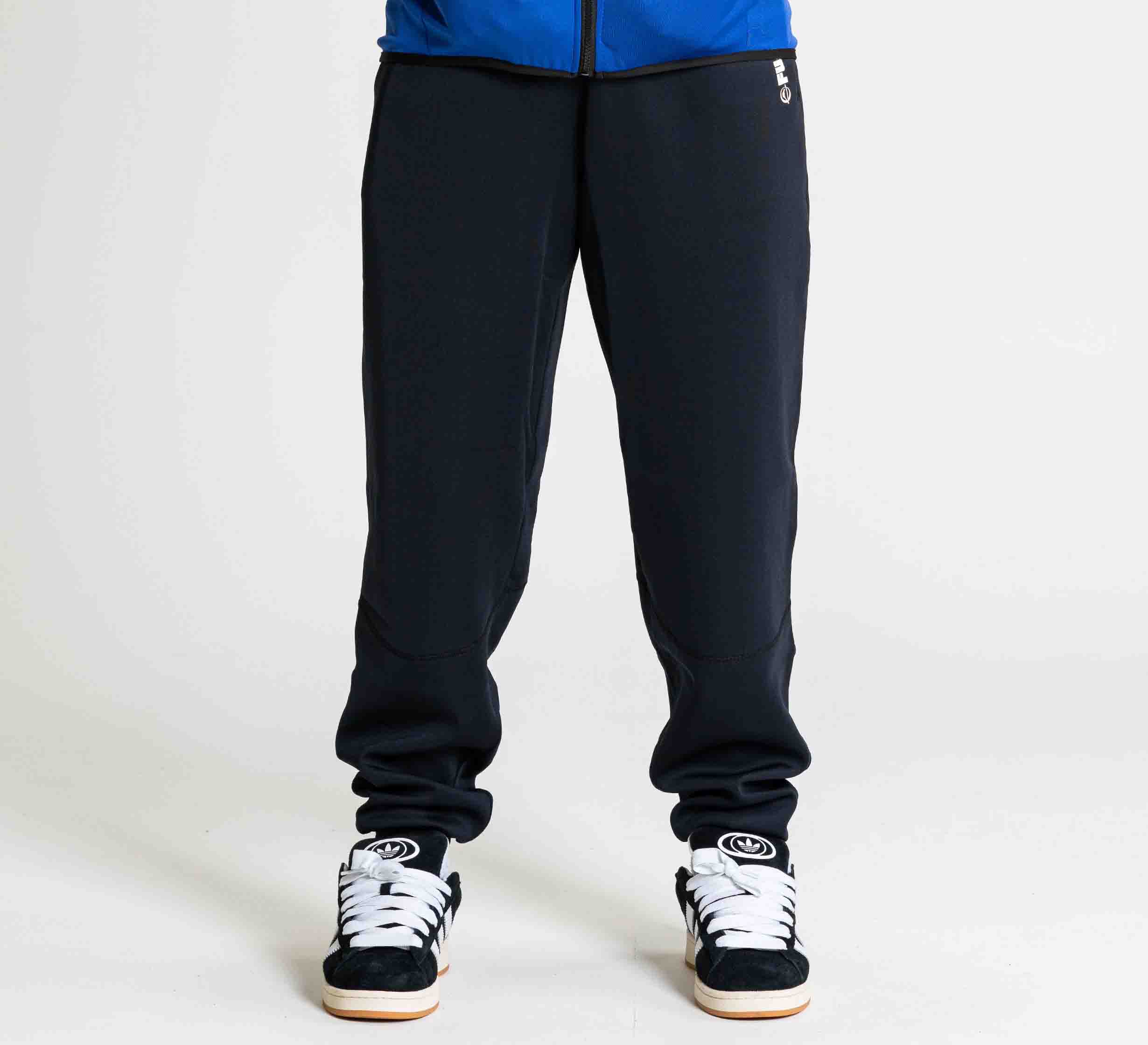 Wearing the FUJI Performance Jogger Black and black sneakers with white soles, a person stands against a plain white background, showing only the lower half of their body.