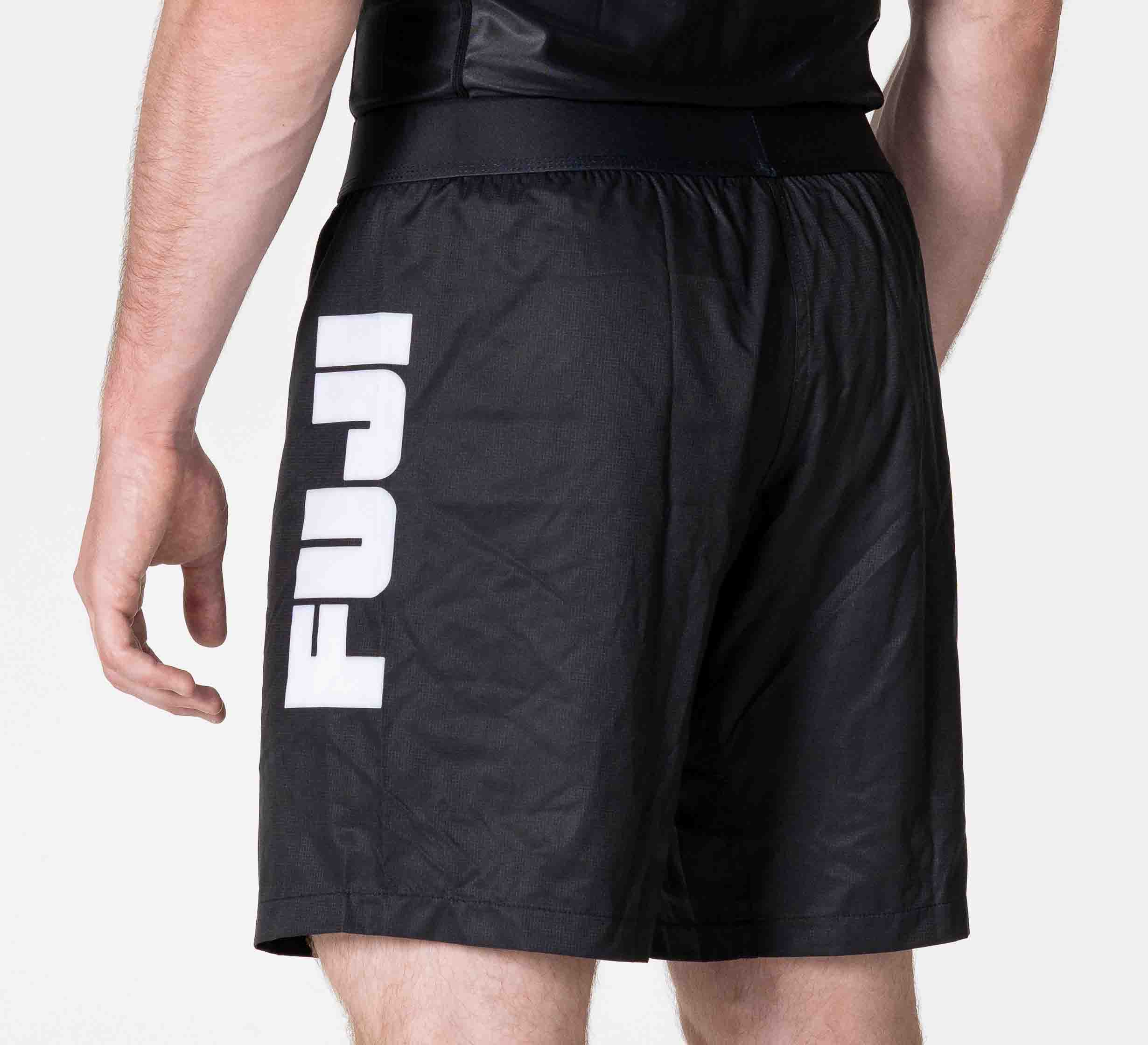 A person is seen from the back and side wearing Competition Ranked Shorts Black, which feature bold white "FUJI" lettering printed vertically on the left leg.