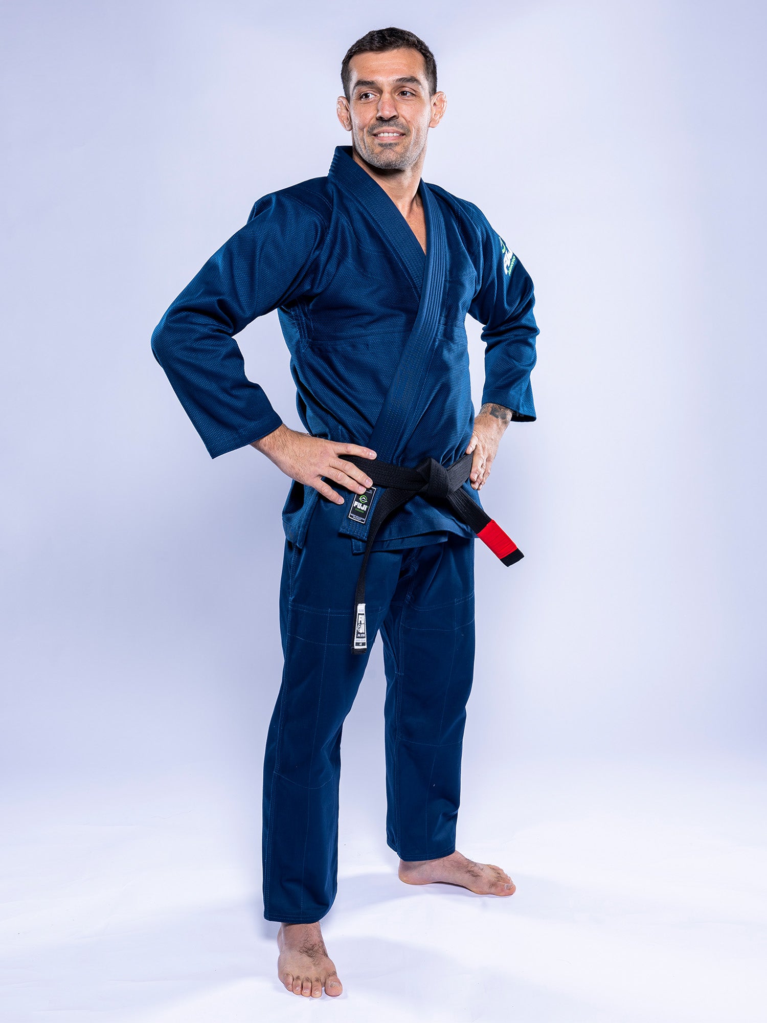 Wearing the Lightweight BJJ Gi Navy and a black belt, a person stands barefoot on a light background, smiling confidently with hands on hips.
