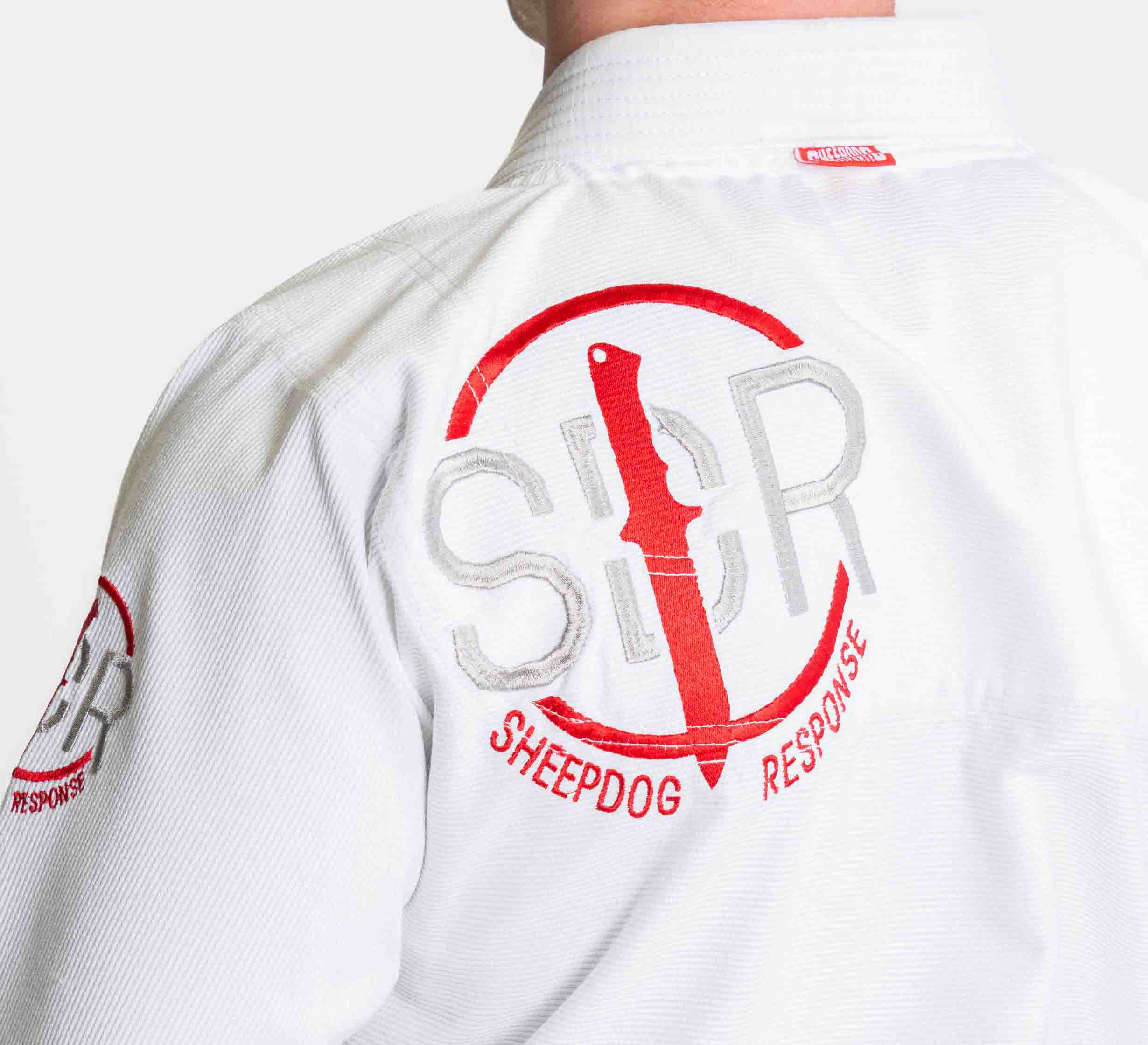 Someone wearing the Suparaito BJJ Gi Sheepdog Response Edition White, featuring SDR and SHEEPDOG RESPONSE embroidered on the back with a red knife and circle logo.