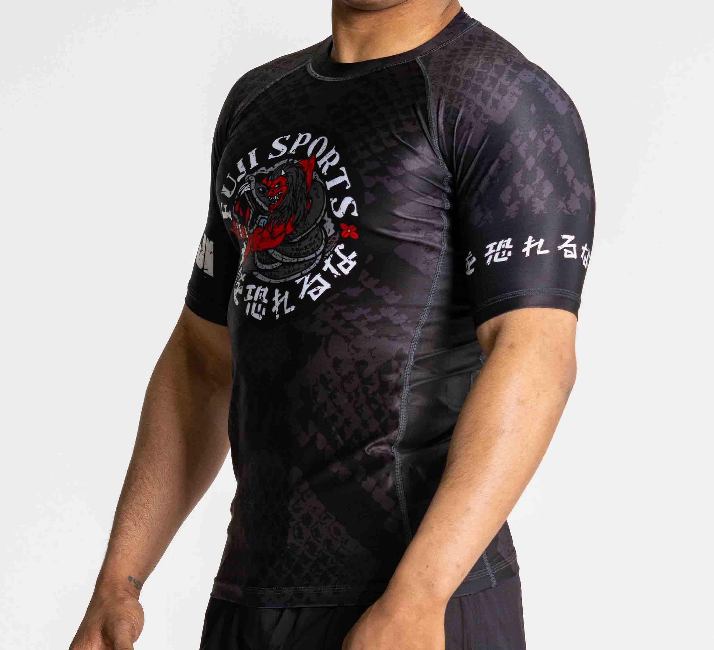 A person wears the Oni vs. Anaconda Short Sleeve Rashguard in black, featuring a dragon graphic, red and white text, and Japanese characters on the sleeve and front. The background is plain white.