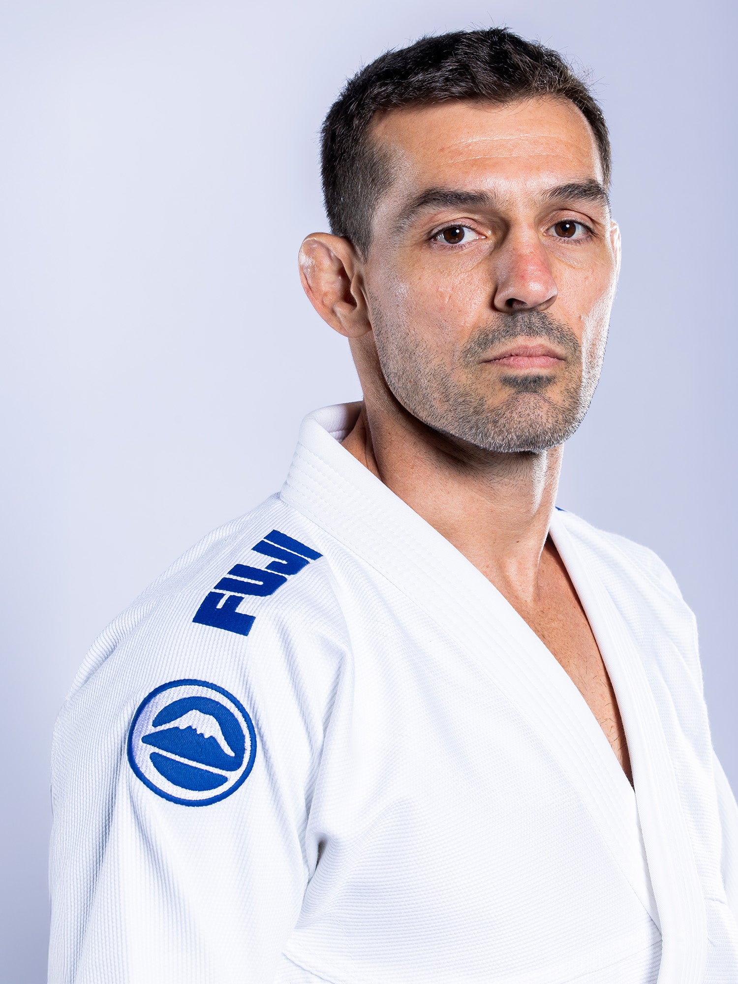 A man with short dark hair and a trimmed beard wears the Baseline 2.0 BJJ Gi White Navy, standing against a plain light background and looking calmly at the camera.