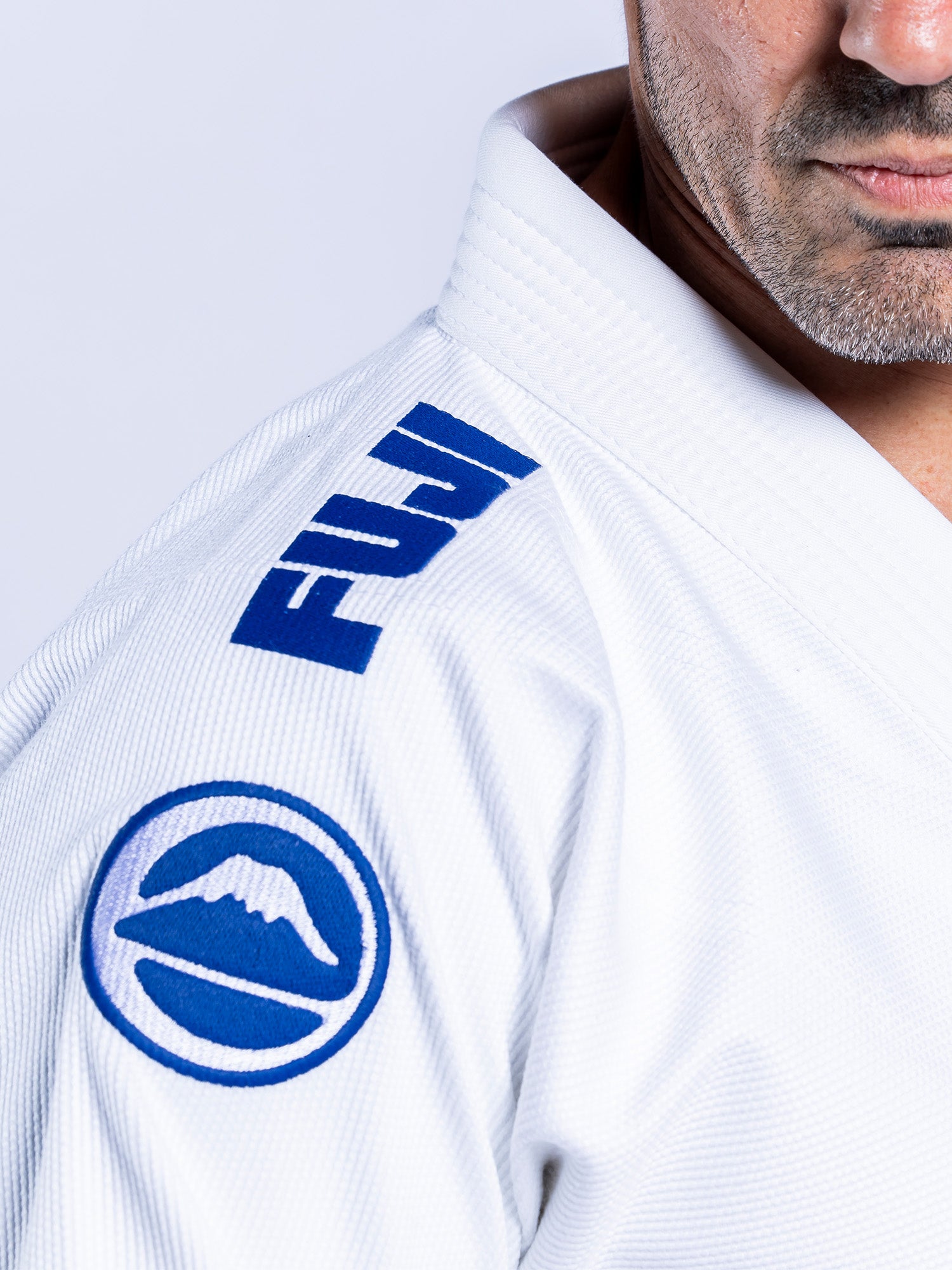 Close-up of a man wearing the Baseline 2.0 BJJ Gi White Navy, featuring a FUJI and blue mountain patch on the shoulder, with part of his face, jawline, and chest visible.