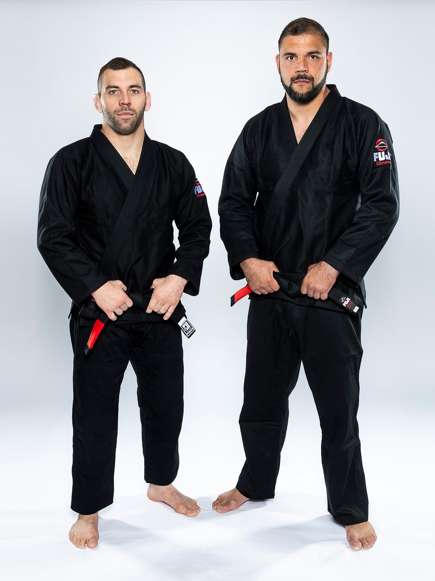 Two men wear All Around BJJ Gi Black uniforms with red-and-black belts, barefoot and facing the camera against a white background with neutral expressions.