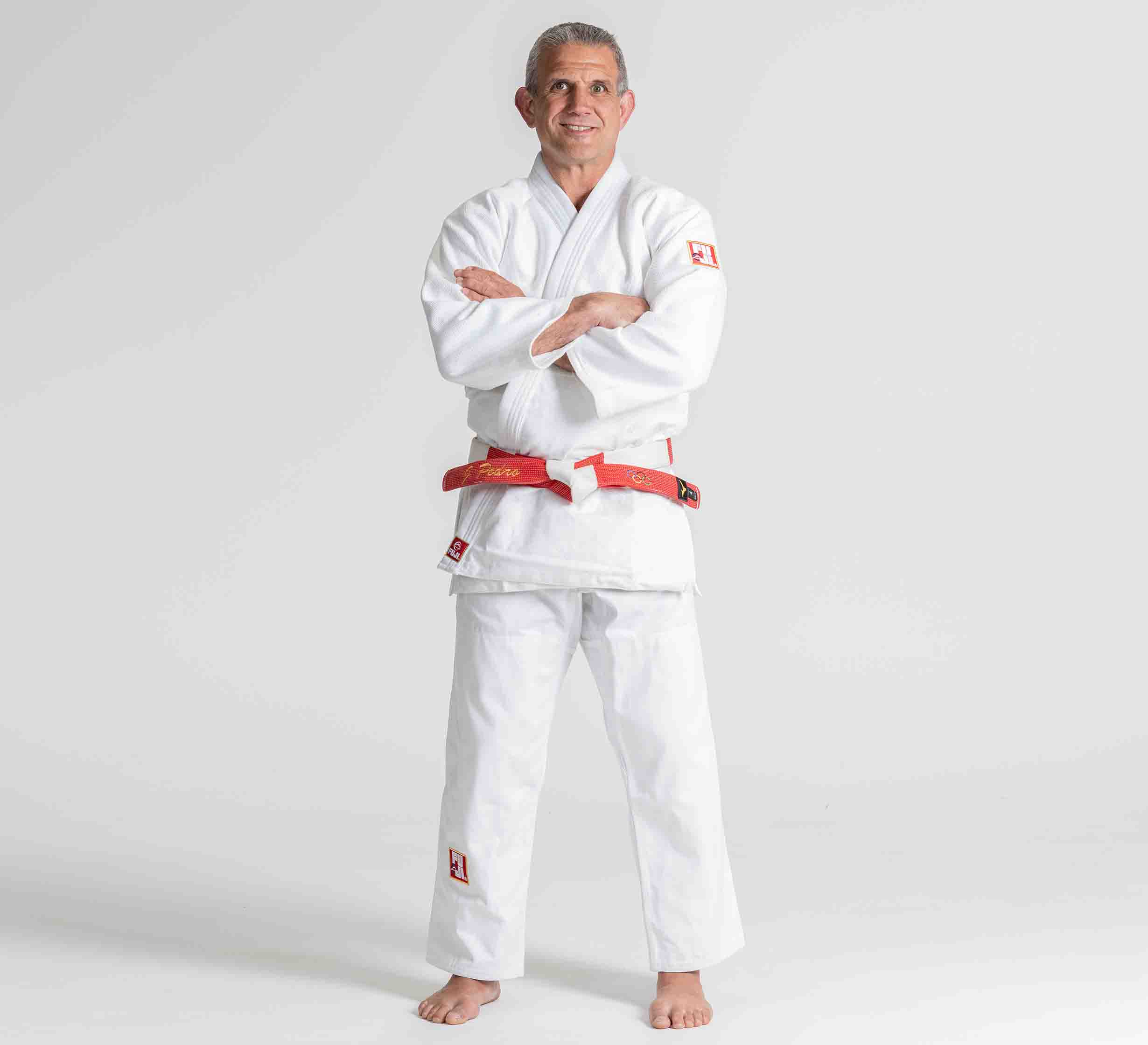 A person wearing the Euro Competition Judo Gi White stands barefoot on a plain background, smiling with arms crossed.