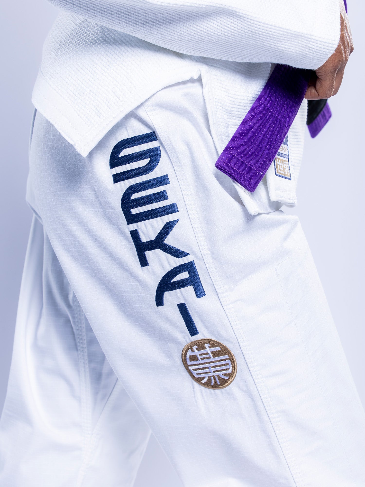 Close-up of a person wearing the Womens SEKAI 3.0 BJJ Gi White Navy with black and gold embroidery on the pants and a purple belt at the waist.