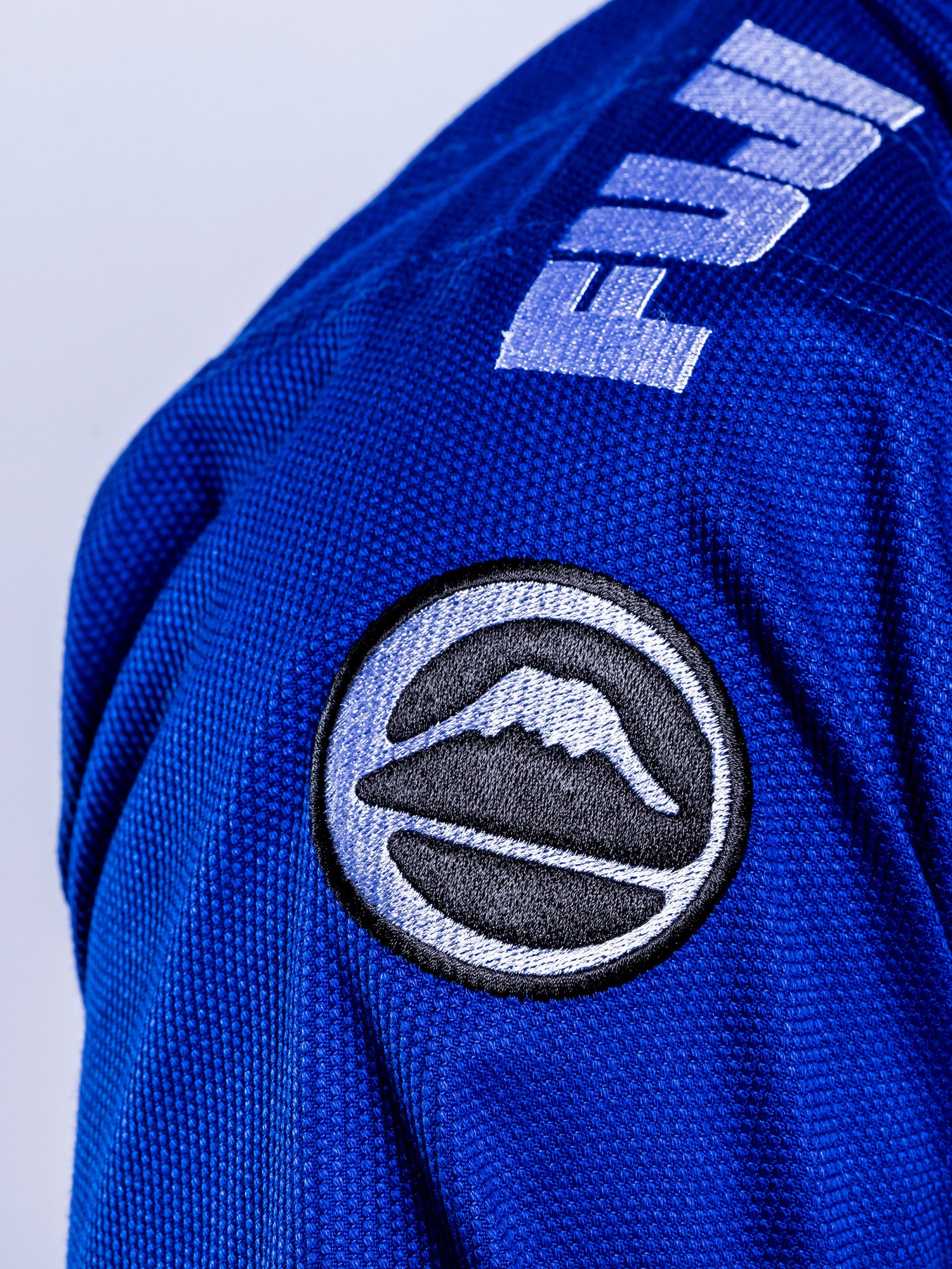 Close-up of the Baseline 2.0 BJJ Gi Blue White, featuring a FUJI logo on the shoulder and a circular Mount Fuji patch.