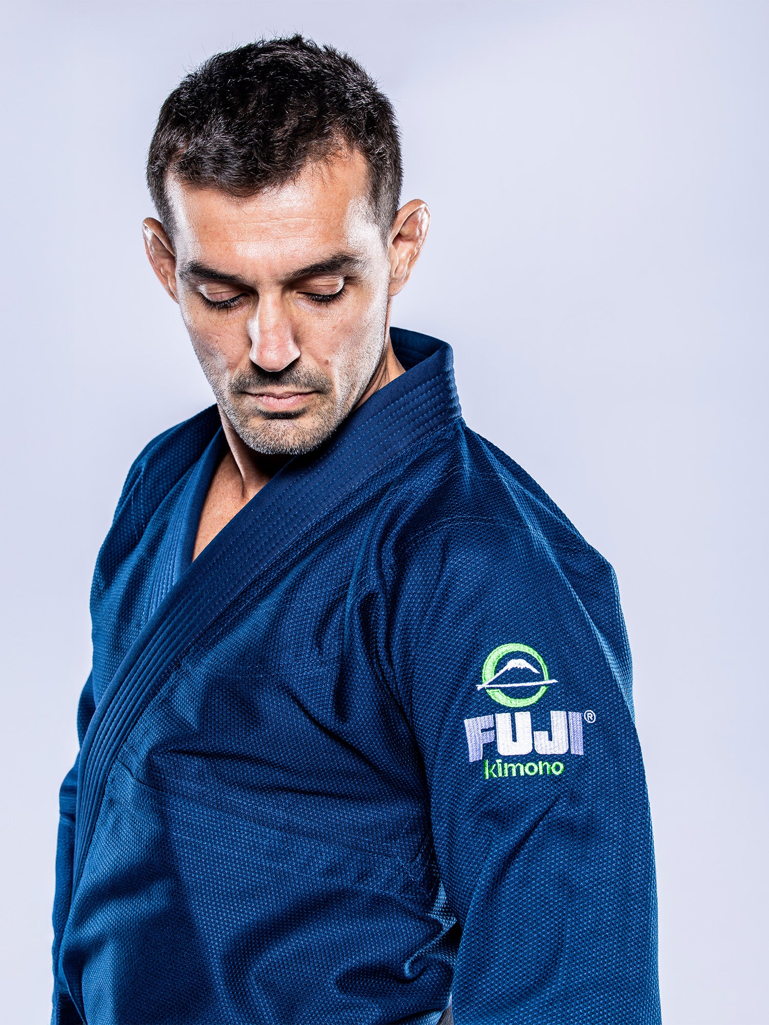 A man wearing the Lightweight BJJ Gi Navy, featuring the FUJI logo on the sleeve, looks down seriously against a light background.