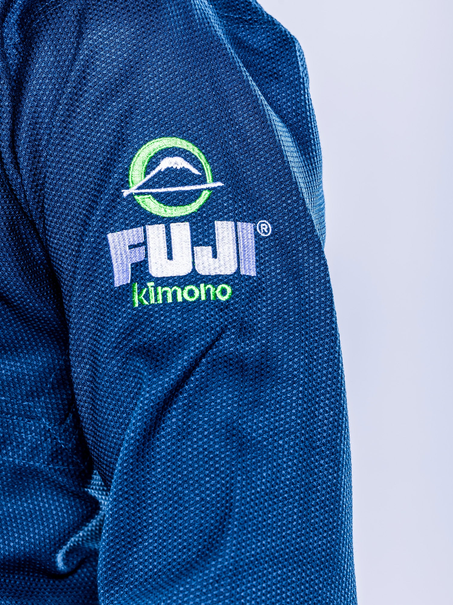 Close-up of the Lightweight BJJ Gi Navy, featuring blue textured fabric with the FUJI Kimono logo and a mountain design embroidered on the sleeve.