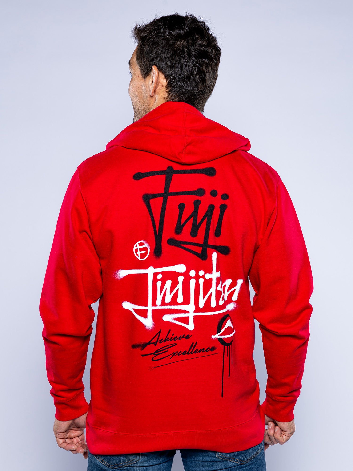 A person is seen from the back wearing the Japanese Street Art Hoodie Red, featuring bold black and white text that reads "Fuji Jiu Jitsu Achieve Excellence" along with stylish graphics.