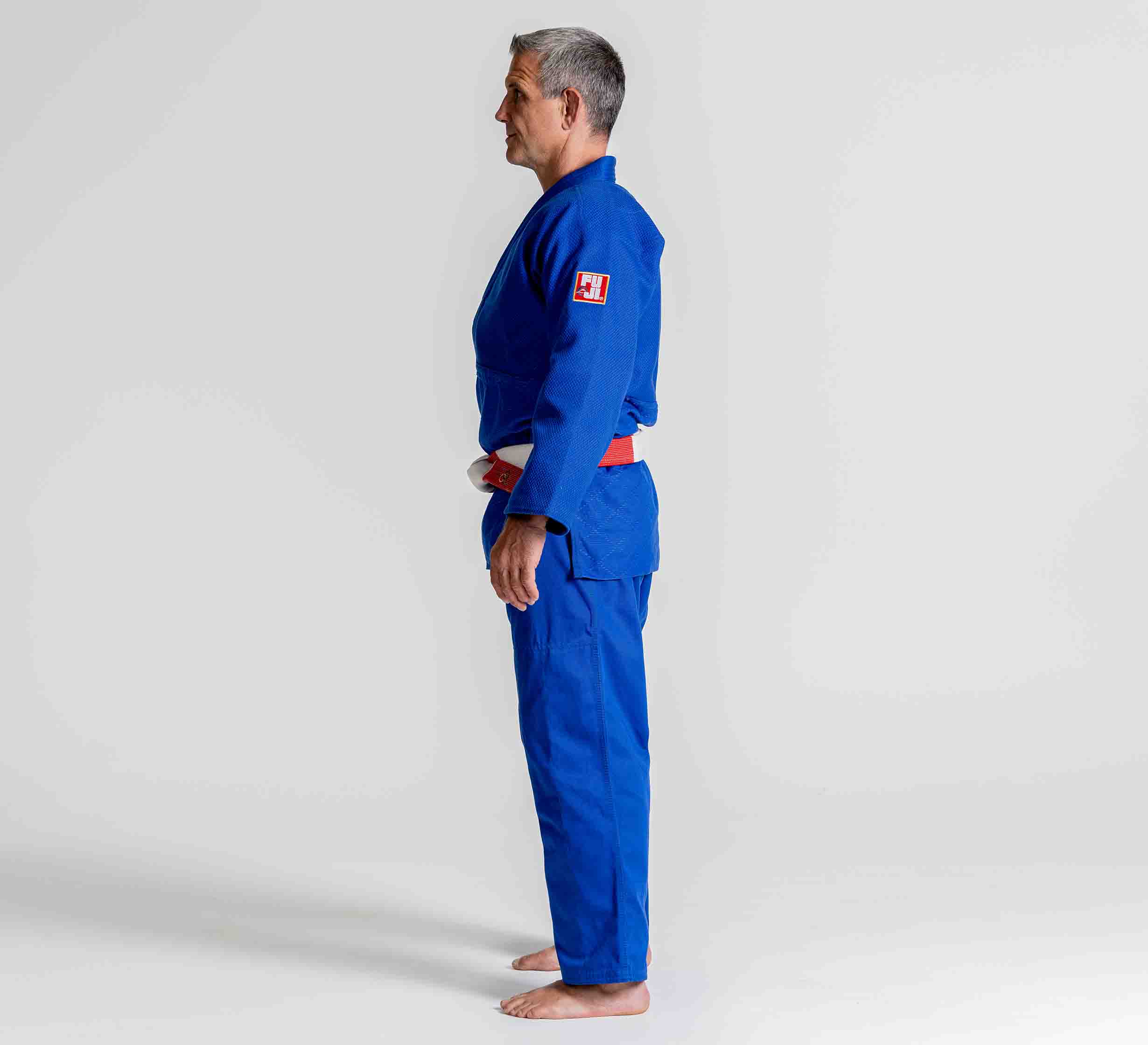 A person wearing the Euro Competition Judo Gi Blue with a red and black belt stands barefoot in profile against a plain white background.