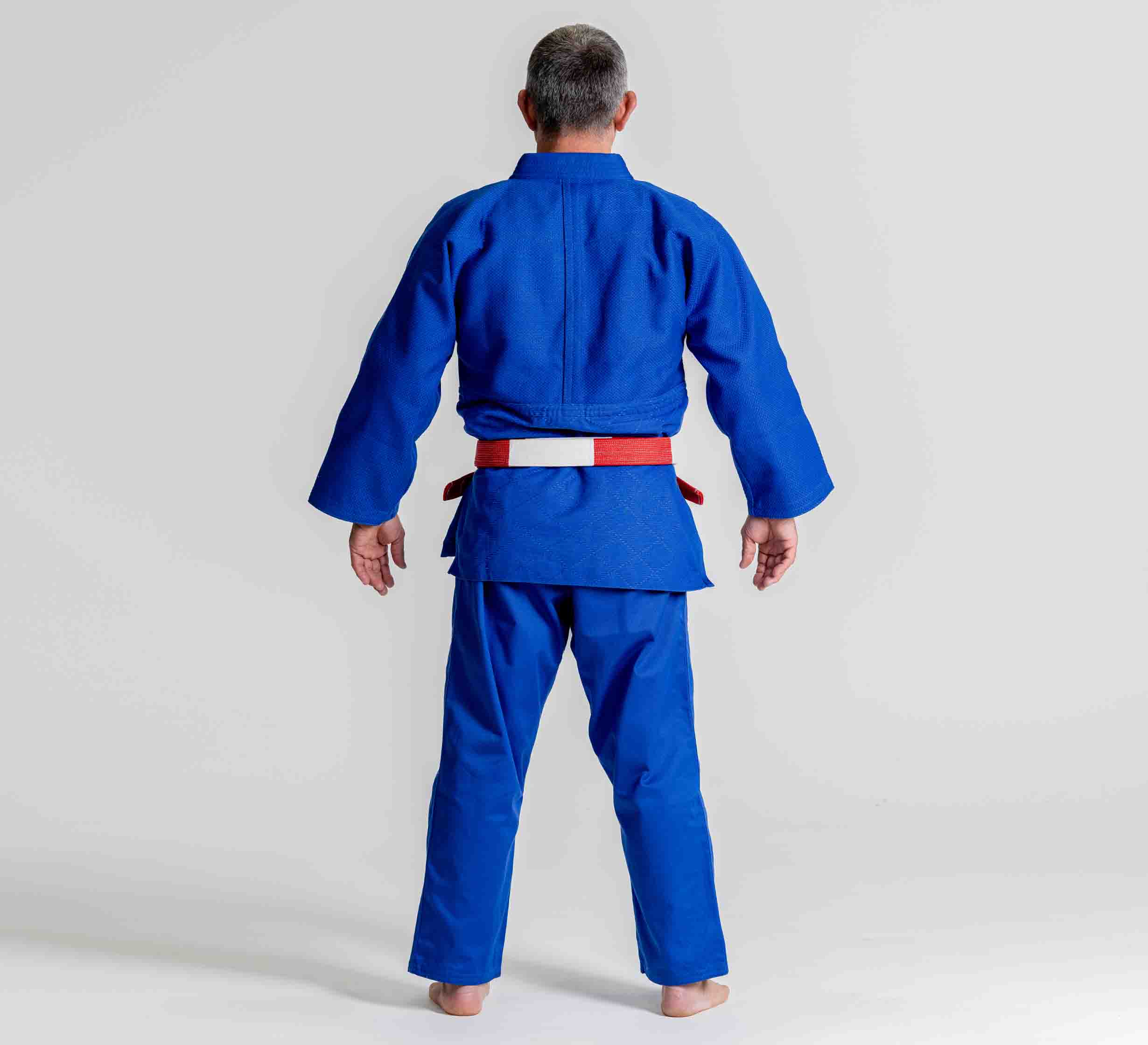 A person wearing the Euro Competition Judo Gi Blue and a red-and-white belt stands barefoot facing away from the camera against a plain white background.