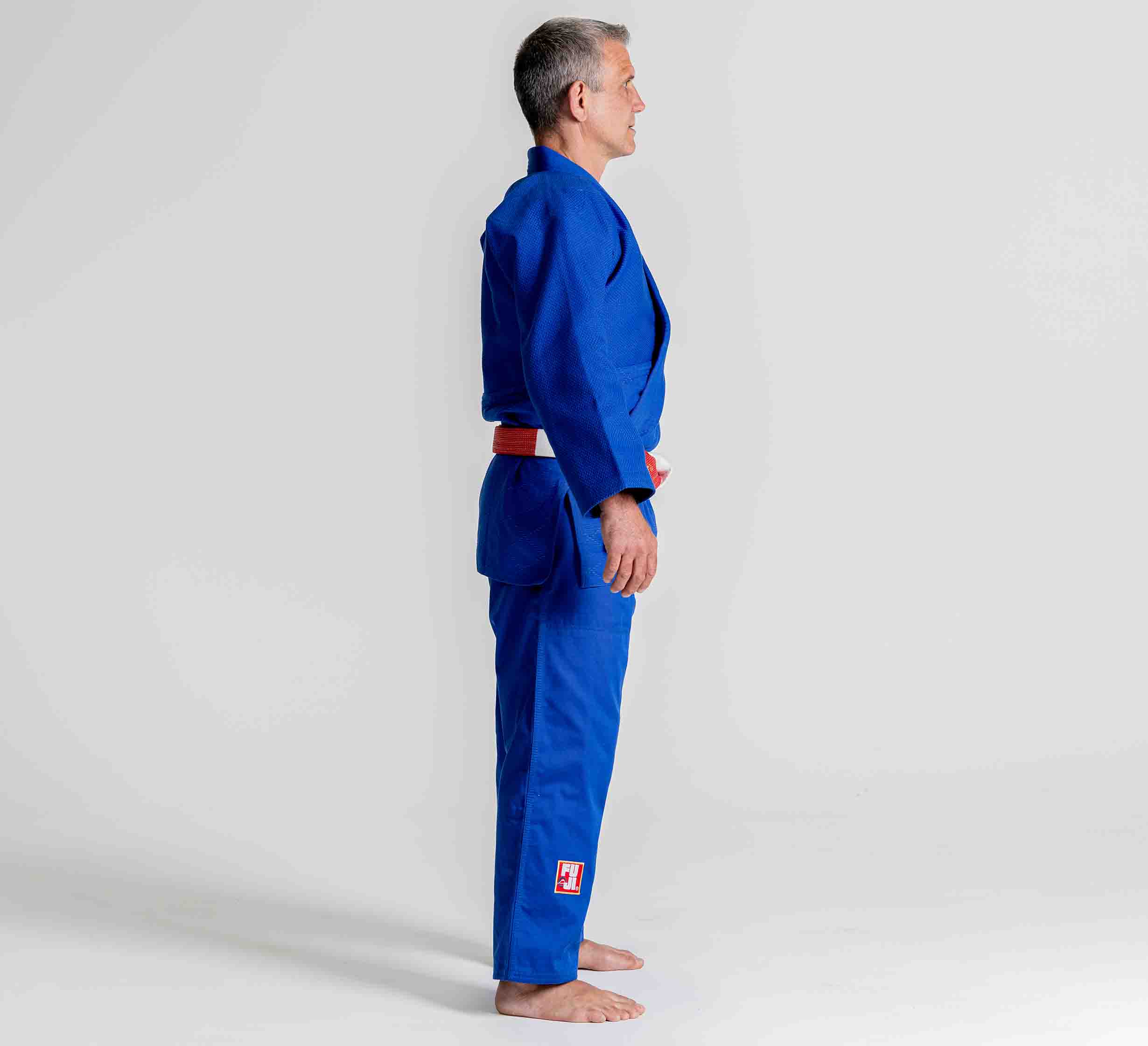 A person wearing the Euro Competition Judo Gi Blue stands barefoot in profile against a plain light background.