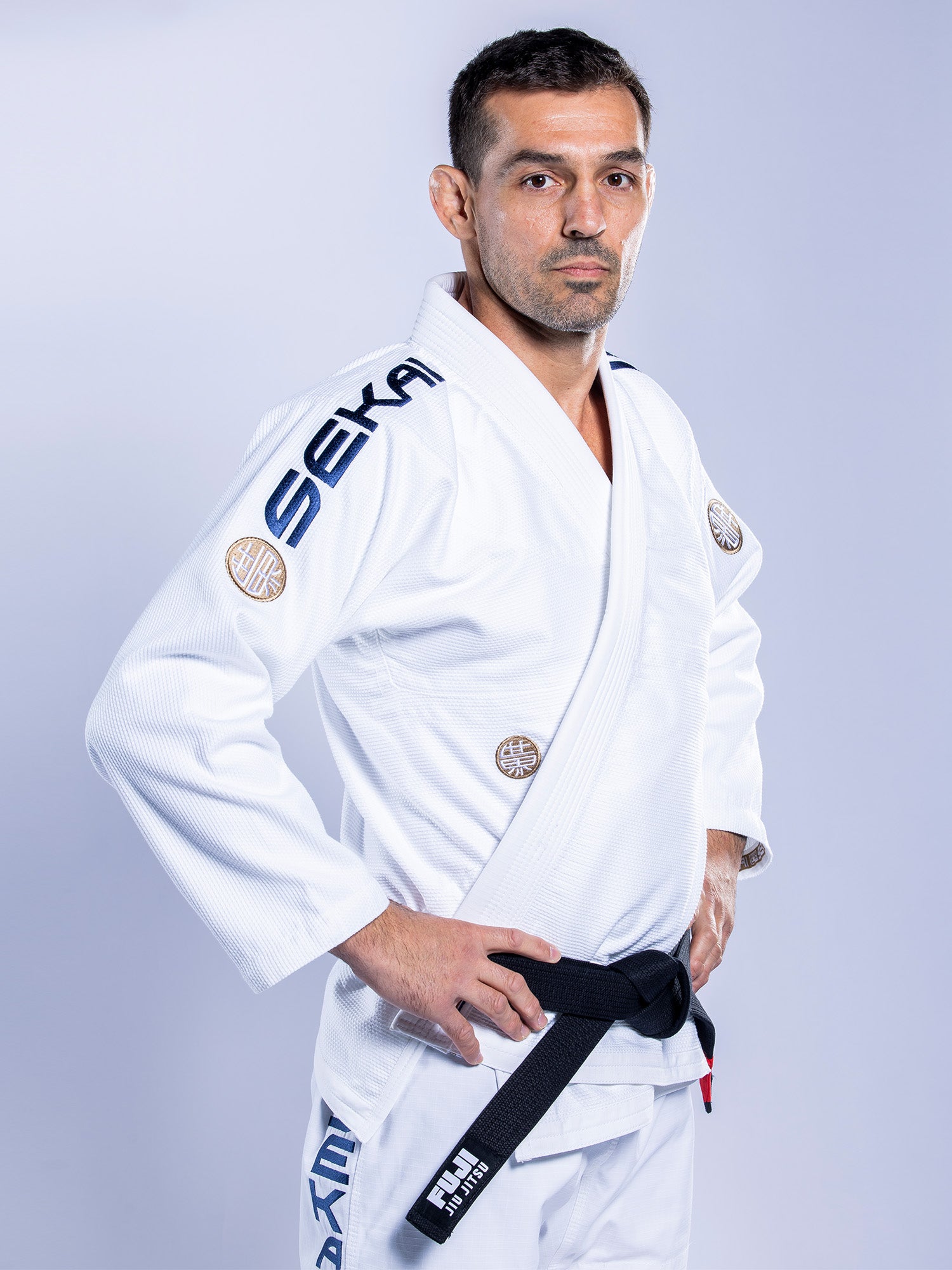 A man stands confidently with hands on hips, wearing the SEKAI 3.0 BJJ Gi White Navy and a black belt, looking at the camera against a plain light background.