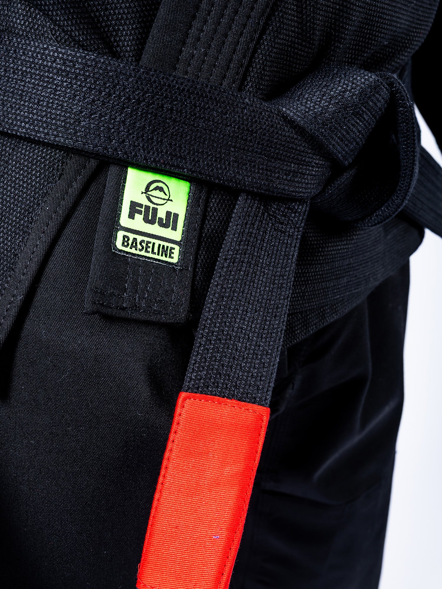 Close-up of a person wearing the Baseline 2.0 Slim Fit BJJ Gi in black with a black belt featuring a green Fuji Baseline label and red tag at the end.