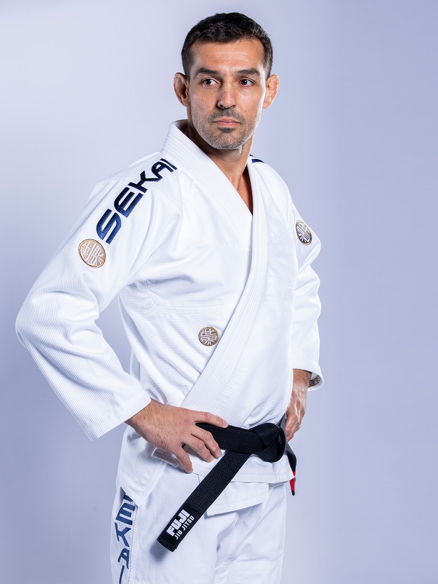 A man stands confidently with his hands on his hips, wearing the SEKAI 3.0 BJJ Gi White Navy and a black belt, looking to the side against a plain light background.