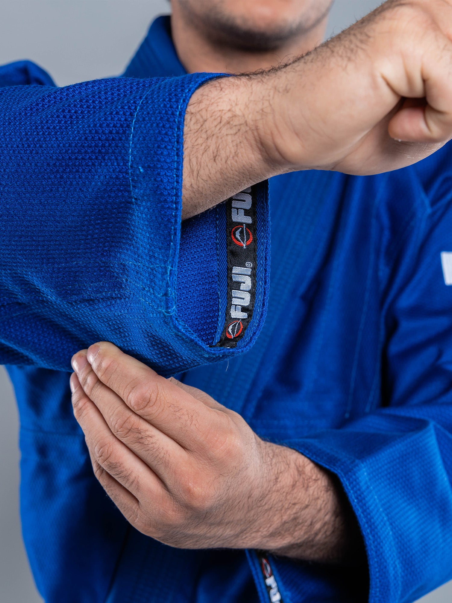 A person folds their arm in a blue Lightweight BJJ Gi, revealing the FUJI brand label inside the sleeve.