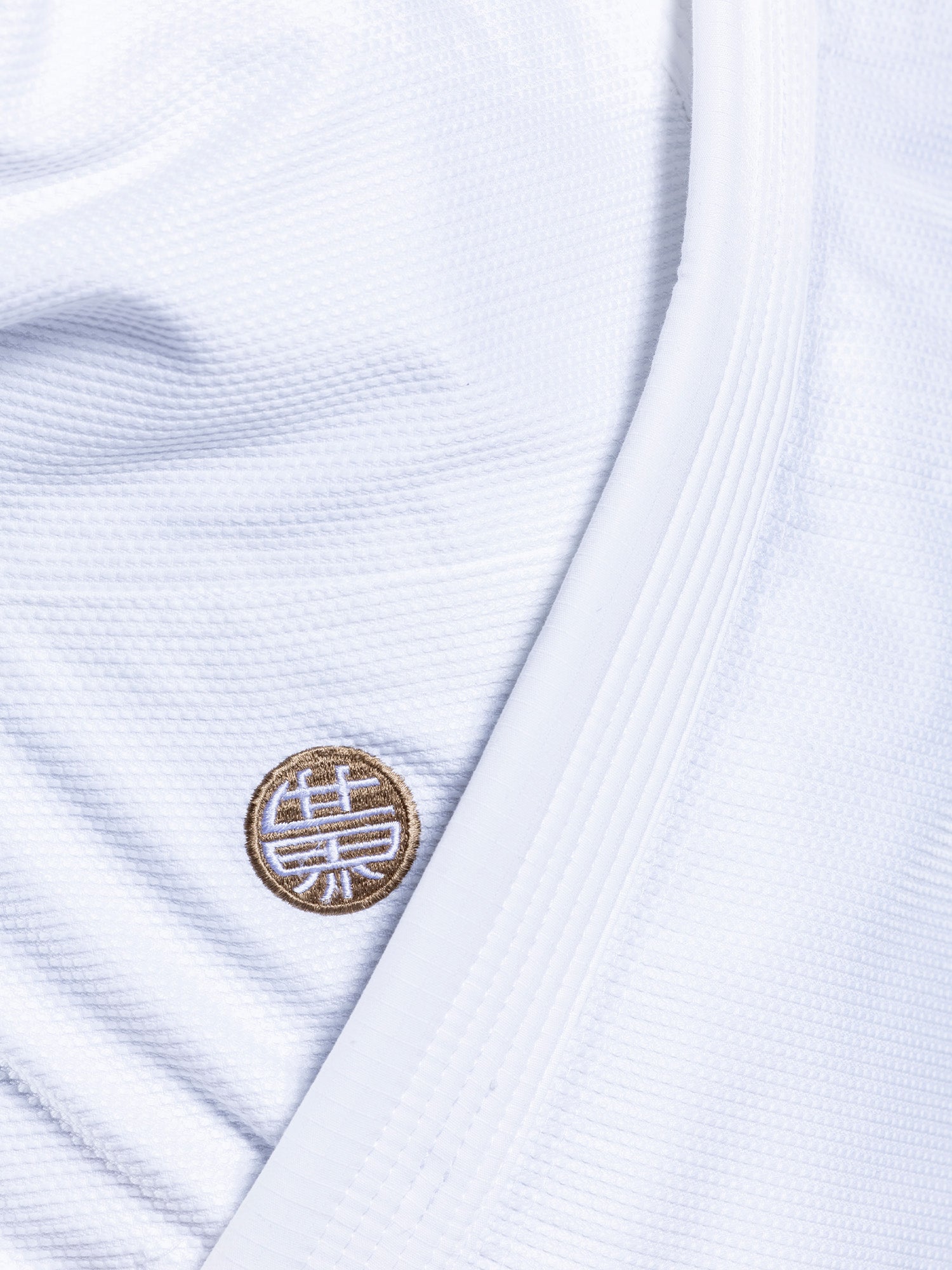 Close-up of the SEKAI 3.0 BJJ Gi White Navy's textured white fabric, showcasing a stitched round patch with a gold and white design inspired by Asian calligraphy, characteristic of this martial arts uniform.