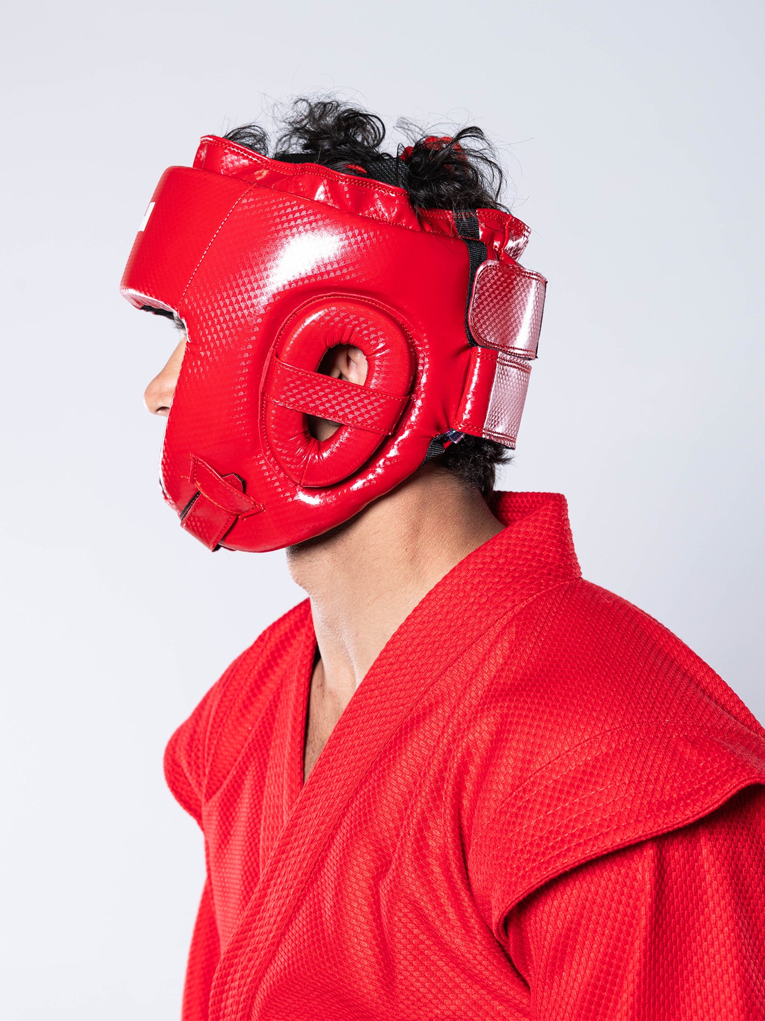 A person wearing a red martial arts gi and the FIAS Sambo Combat Headgear Red is shown in profile against a plain light background.