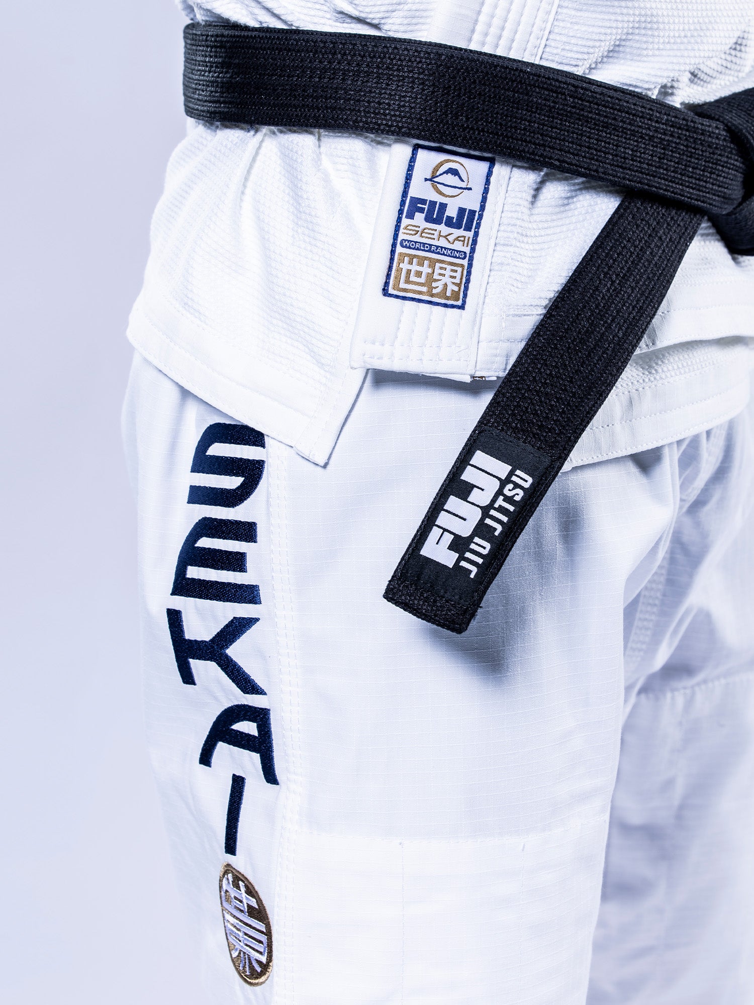 A person wears the SEKAI 3.0 BJJ Gi White Navy with a black belt. The gi features FUJI SEKAI patches on the jacket, SEKAI and FUJI JIU JITSU patches on the pants, and visible Japanese characters.