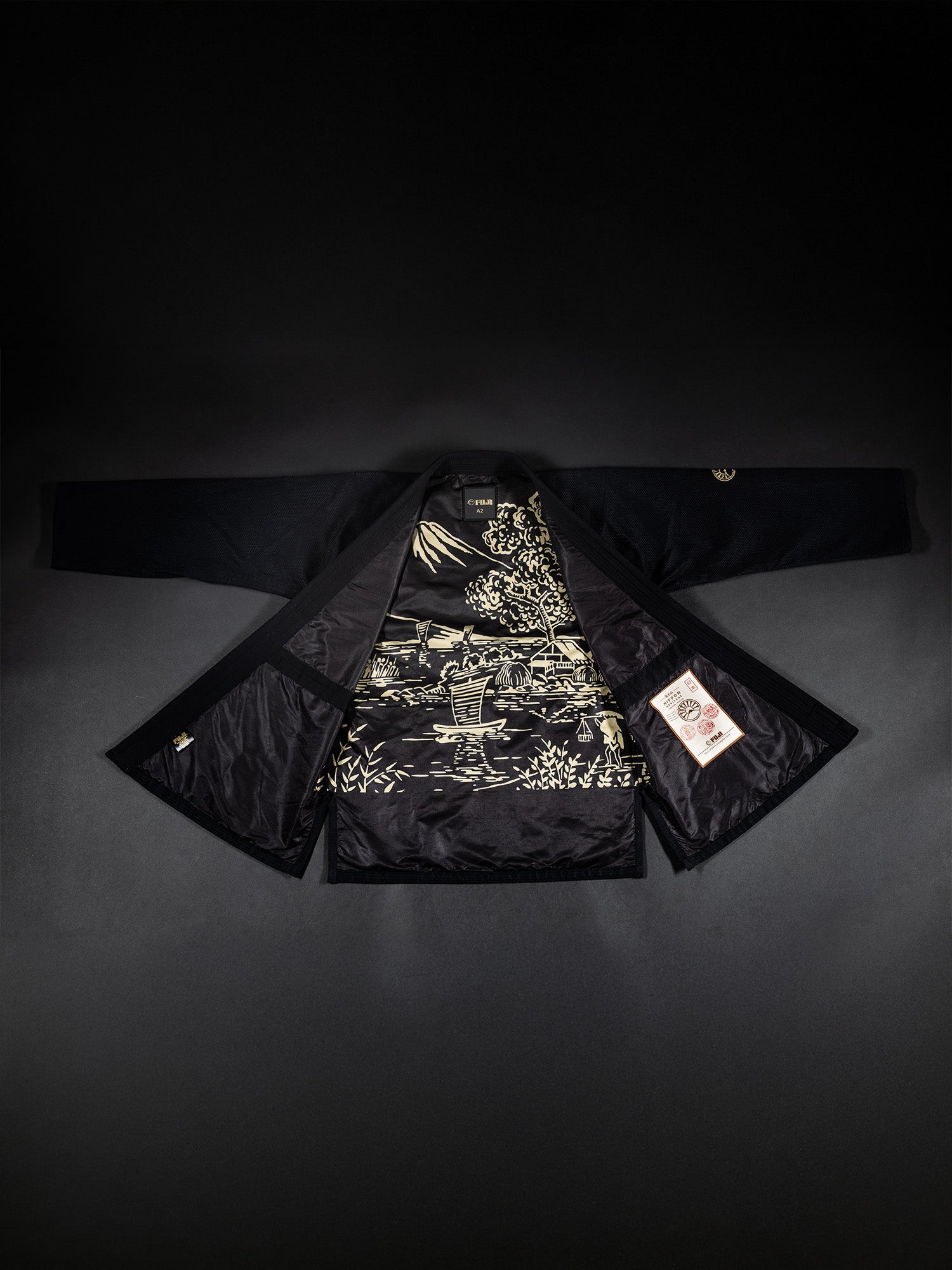 The Heritage Keisho Lightweight BJJ Gi Black is laid flat on a dark surface with its sleeves extended. The interior lining showcases an intricate gold landscape design, and there is a white tag with red text on the right inner side.