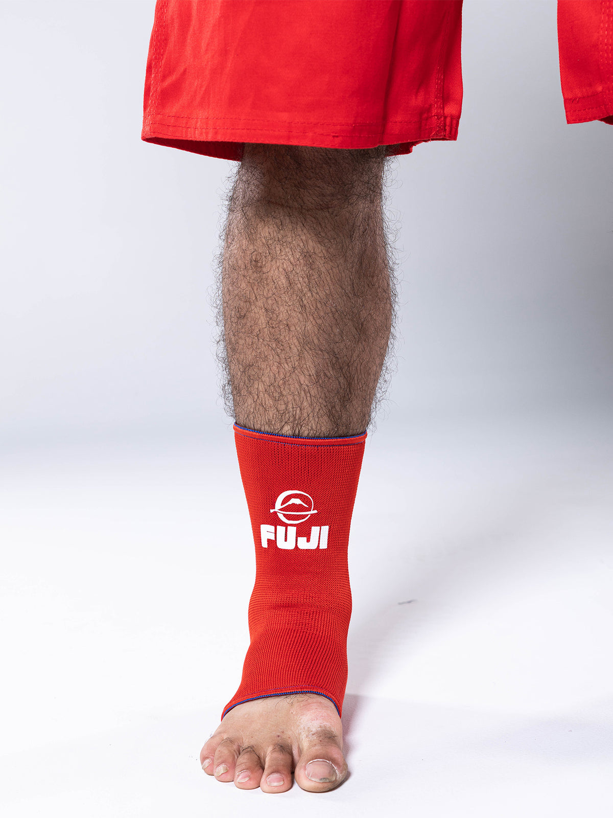 A person wearing red shorts and a red FIAS Sambo Beach Ankle Support Reversible stands on a white surface, showing their bare foot and lower leg.