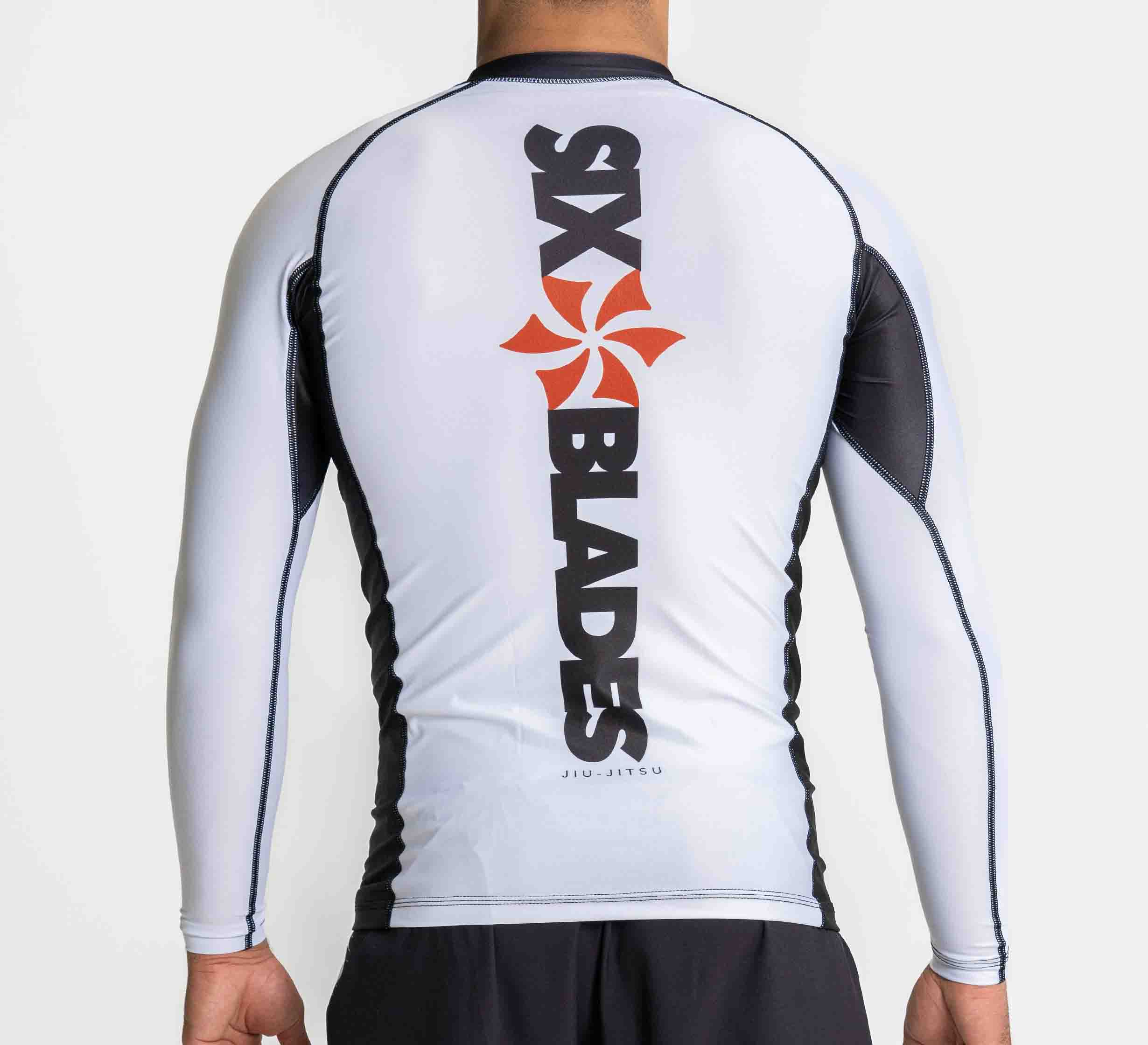 A person is seen from behind wearing the Six Blades Long Sleeve Rashguard White, featuring black sleeves and an orange vertical logo on the back.