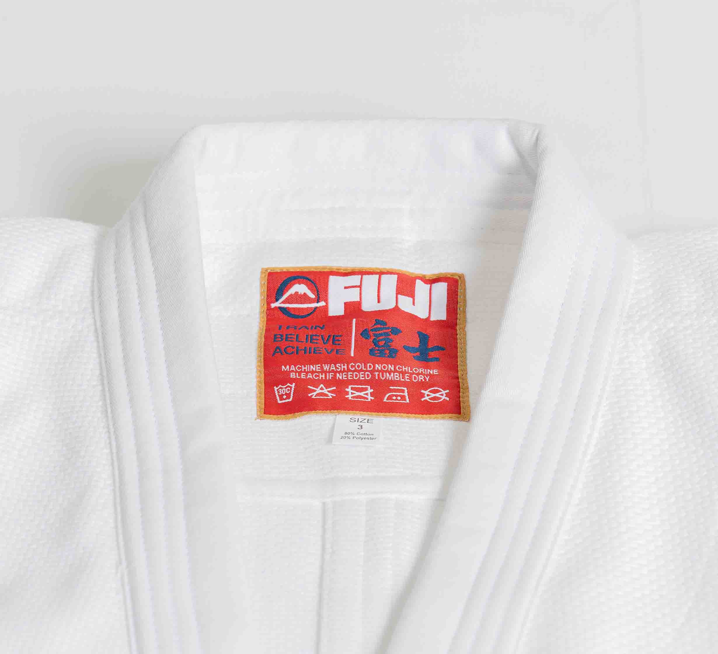 Close-up of the Euro Competition Judo Gi White featuring a red FUJI label on the collar with “BELIEVE | ACHIEVE,” care instructions in English and Japanese, and multiple laundry care symbols.