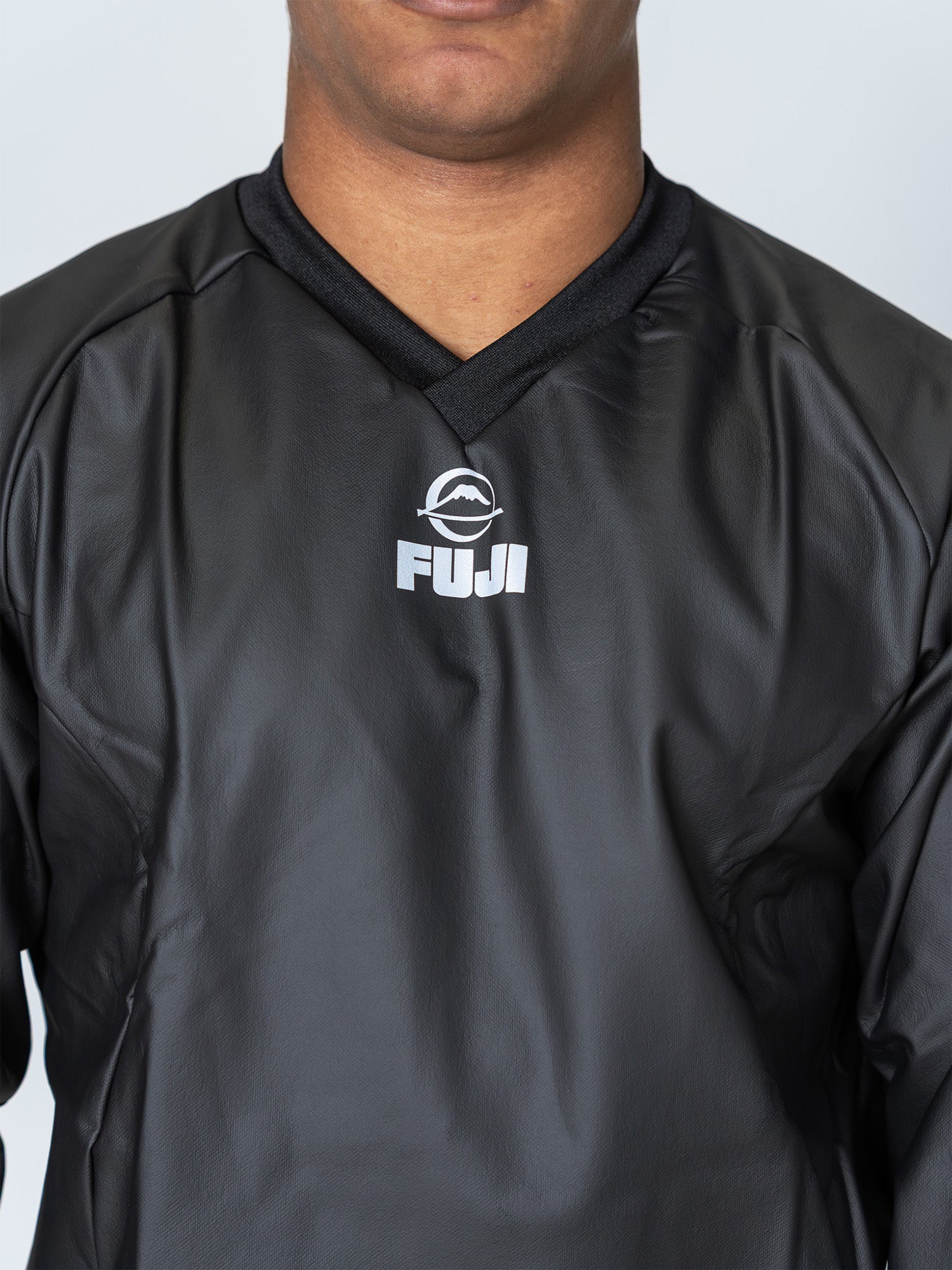 A person is wearing the Grappling Sauna Suit Black, featuring a black V-neck design with the FUJI logo in white on the chest. The image shows only the lower face and upper torso, cropped at the shoulders and just above the mouth.
