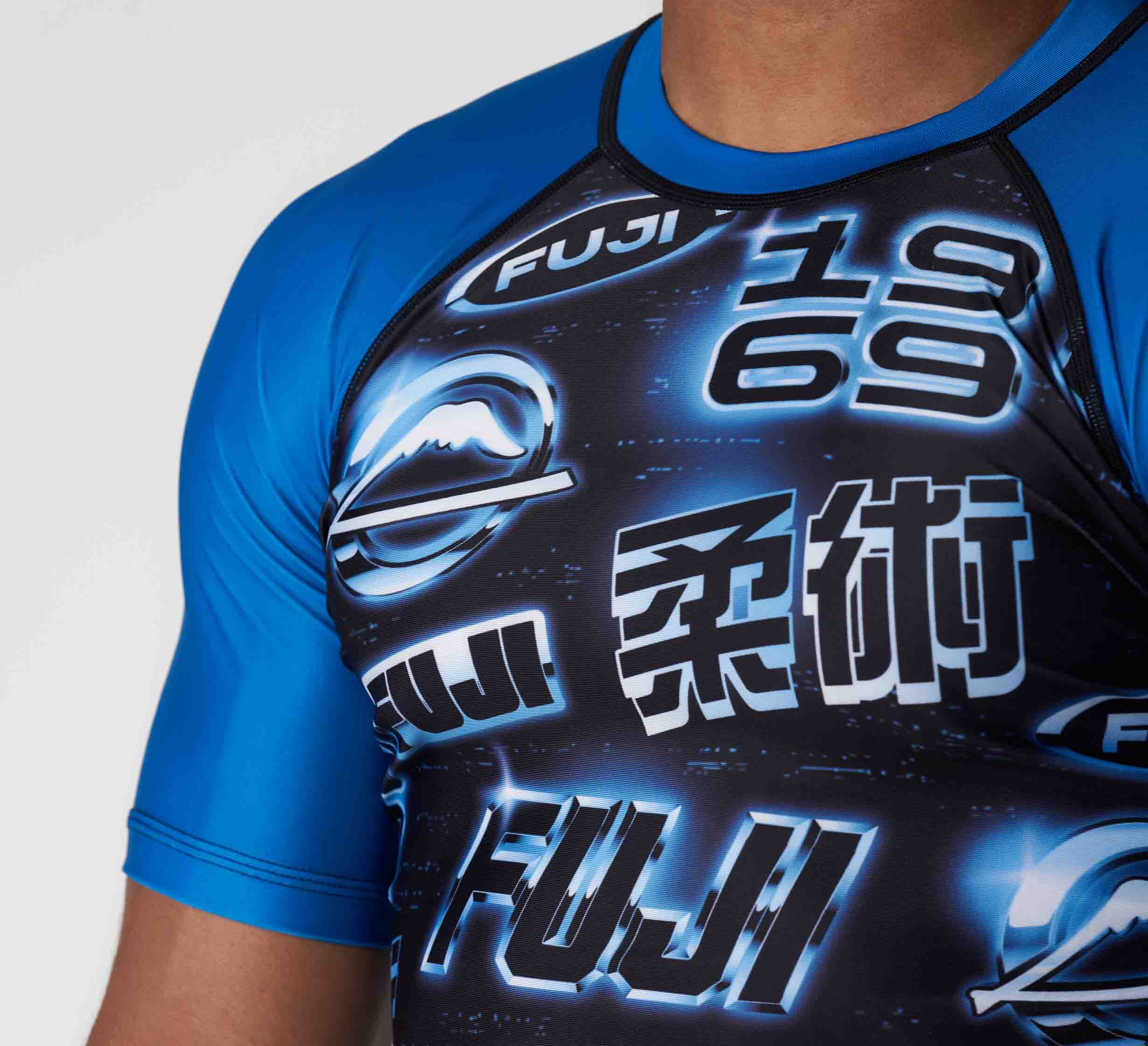 A person wearing the Synth Flex Lite Rashguard Blue, a short-sleeve athletic shirt with neon designs featuring "FUJI," "1969," and Japanese kanji on the chest.