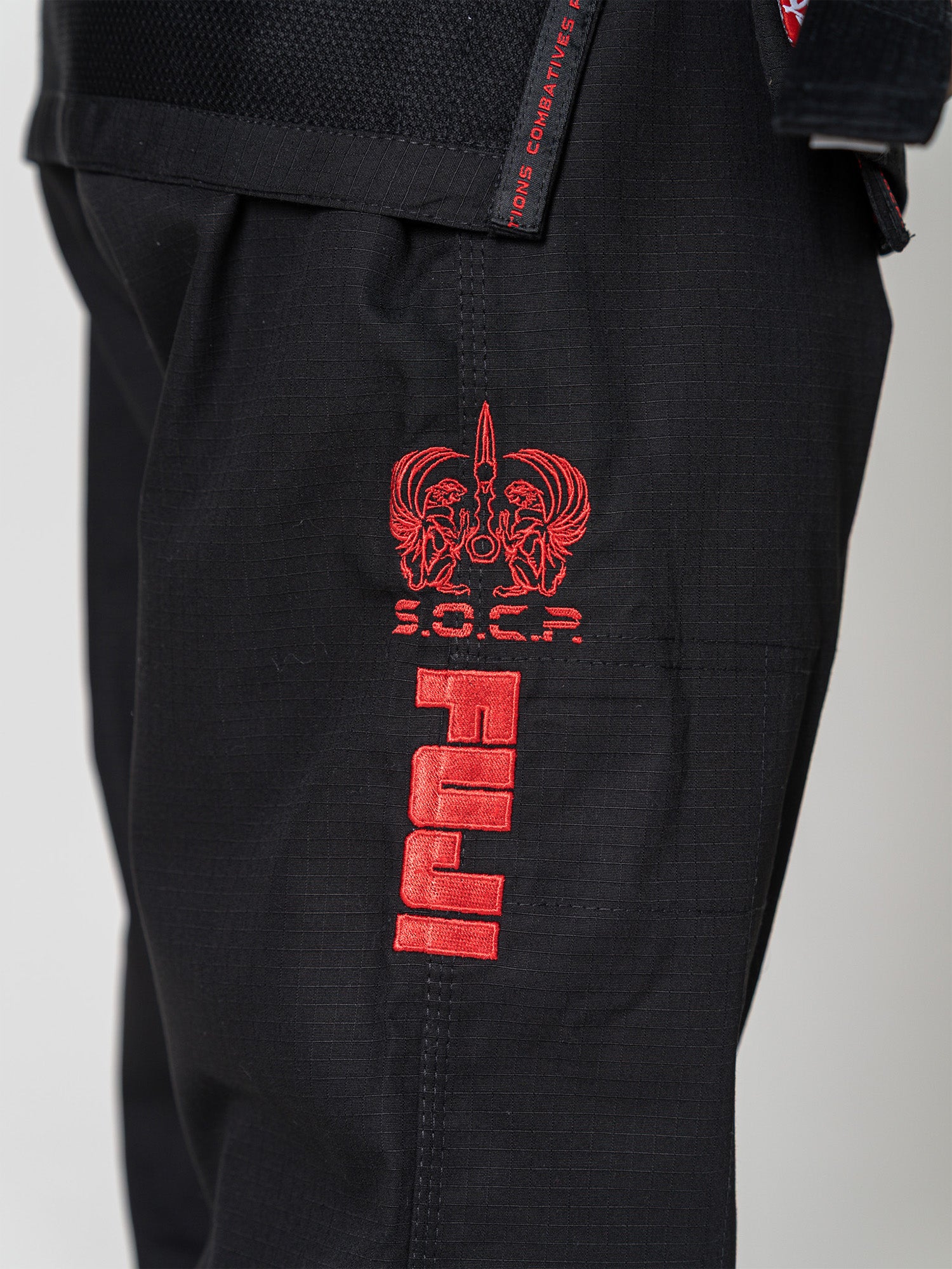 Close-up of the S.O.C.P. Sekai BJJ Gi 2.0 Black, showing red embroidered eagle logo and "S.O.C.P." lettering on the pants above bold vertical red text.