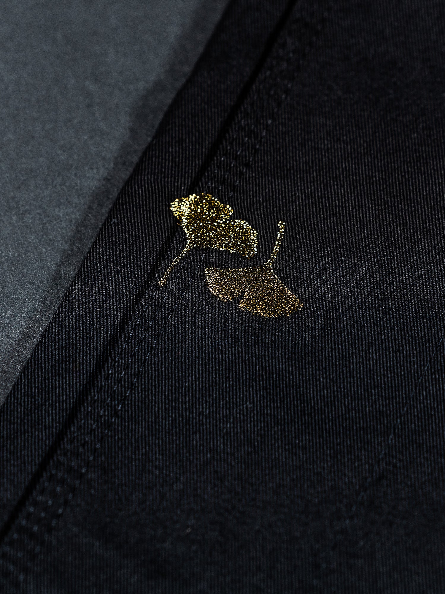 Close-up of a small gold butterfly design on the Womens Heritage Keisho Lightweight BJJ Gi Black, showing visible stitching and a soft shadow along the seam.