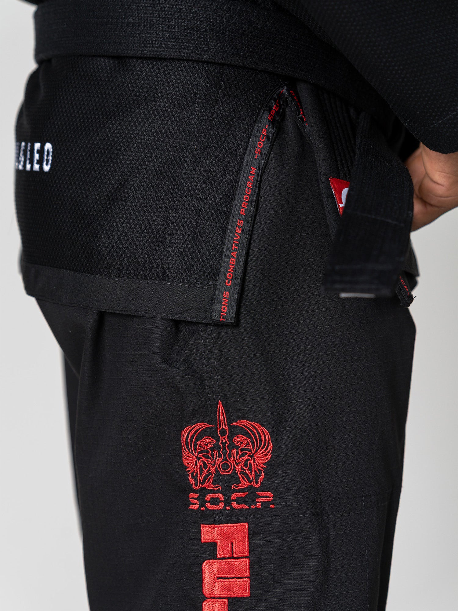 Close-up of a person wearing the S.O.C.P. Sekai BJJ Gi 2.0 Black, featuring red embroidery, detailed logo, “S.O.C.R.” text, and a partially visible black belt.