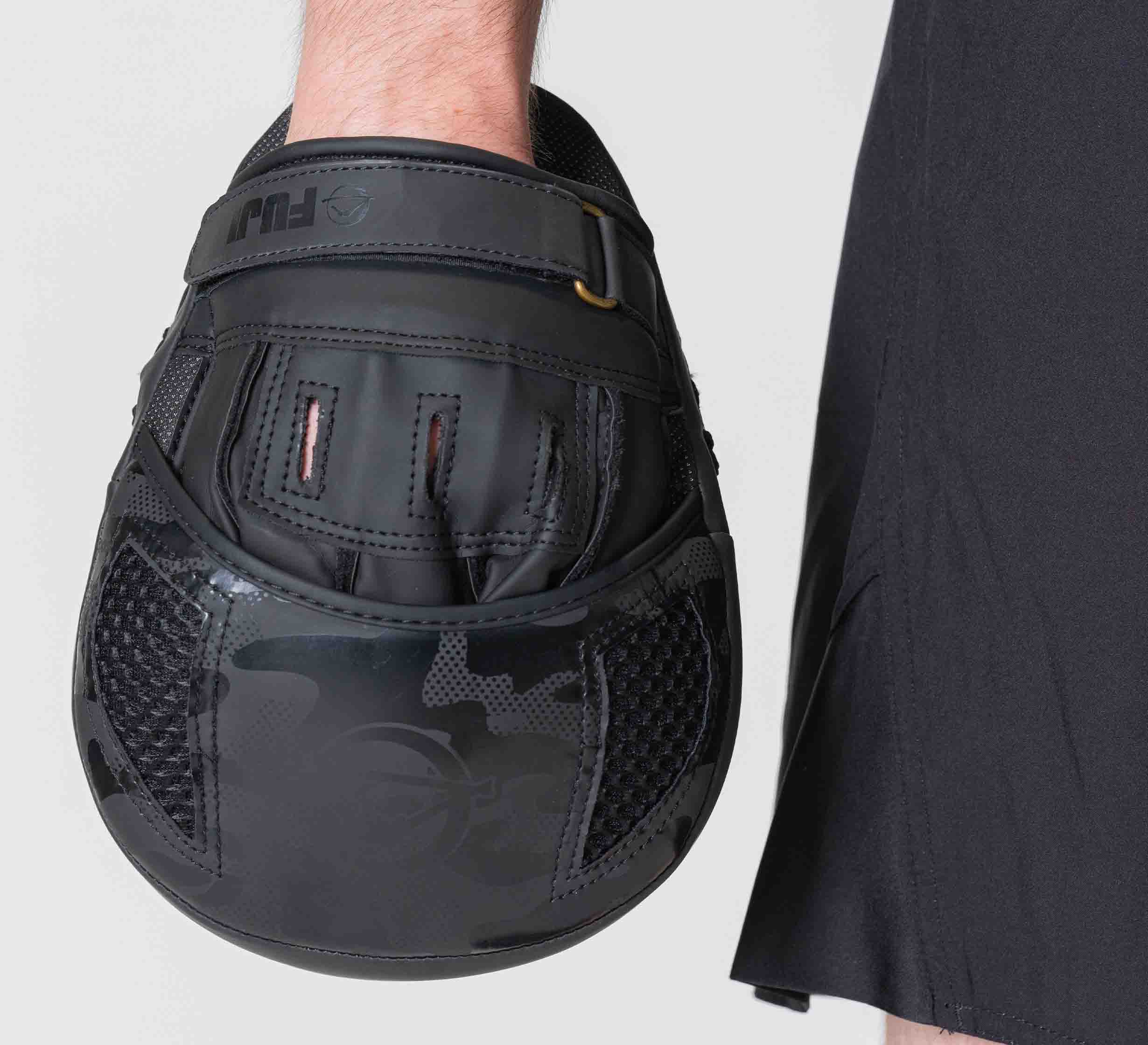 A person holds their arm relaxed by their side wearing Raijin Focus Mitts next to black shorts, all set against a plain light background.