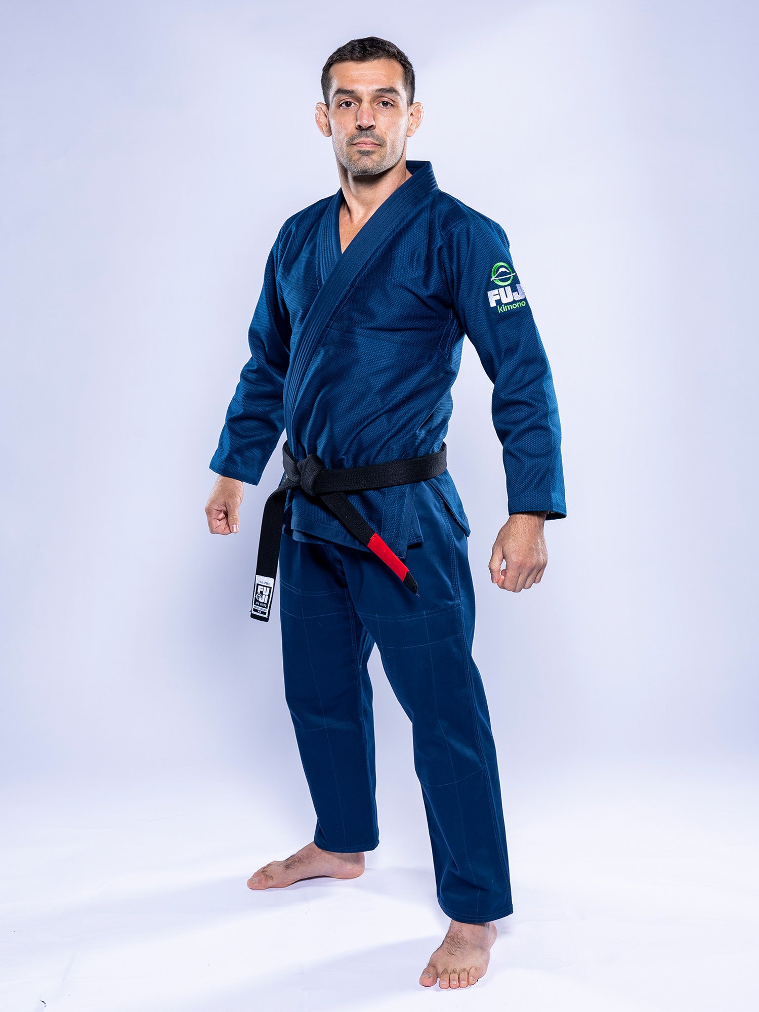 A man stands confidently, barefoot and facing forward, wearing the Lightweight BJJ Gi Navy with a black belt against a plain light background.
